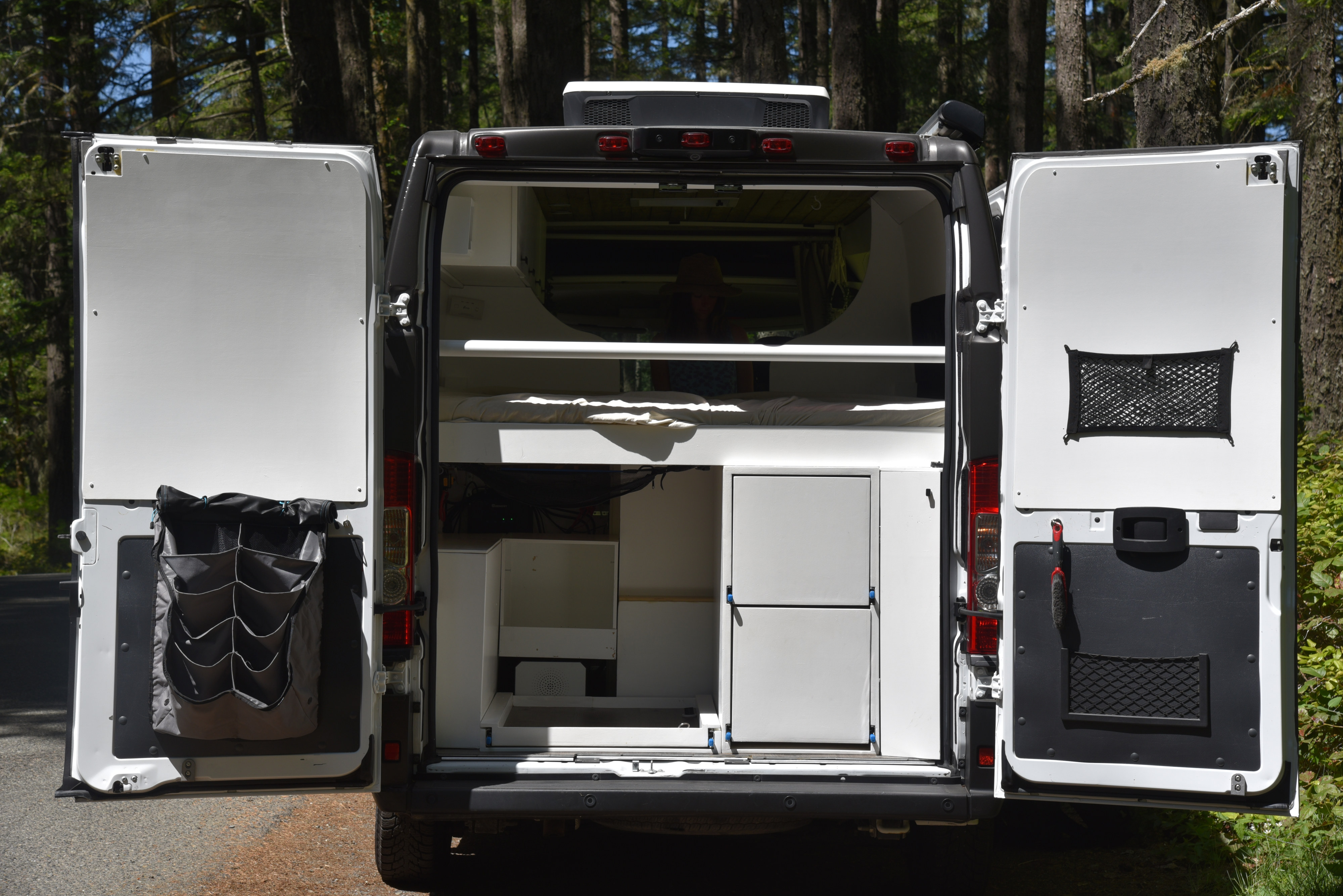 Back of an RV rental with open doors shows a camper van's custom interior: bed, storage, and door organizers.. Ram Promaster 2019
