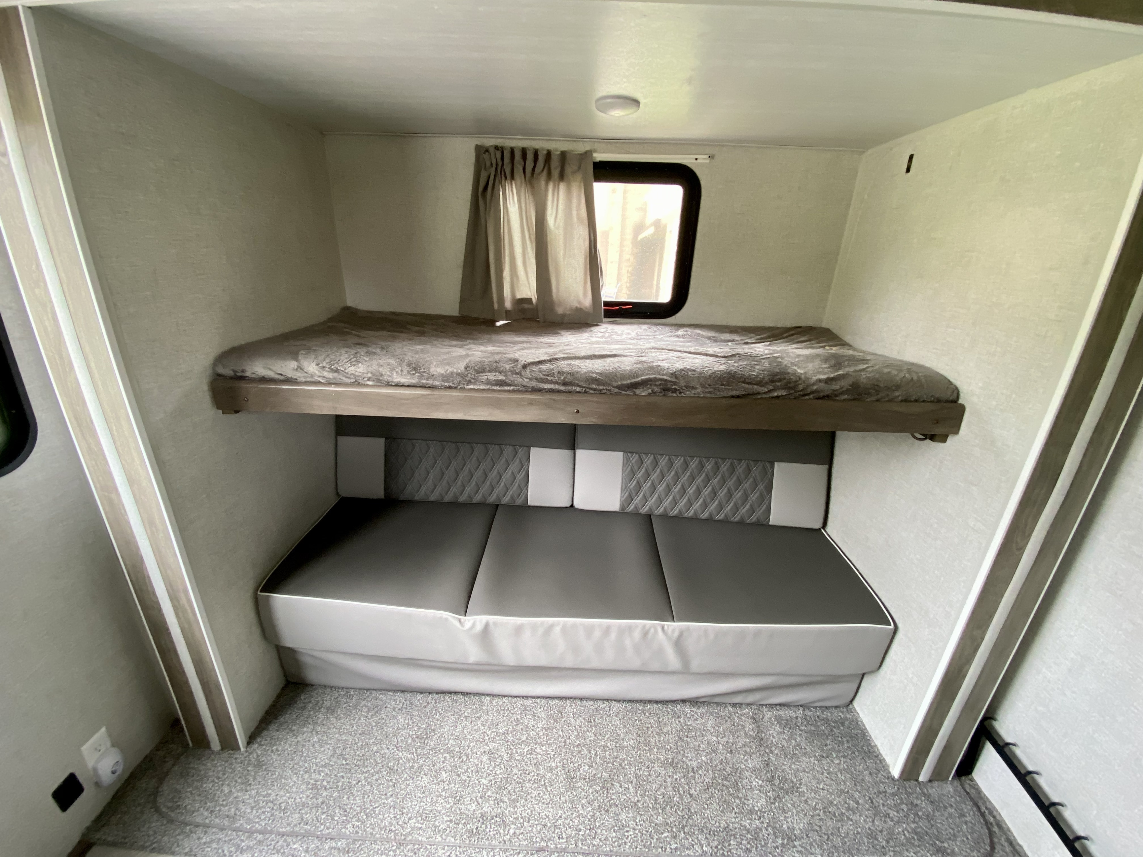 Comfortable RV rental interior features a bunk bed over a gray sofa/dinette, with a window and carpeted floor.. wildwood 32BHDS 2021