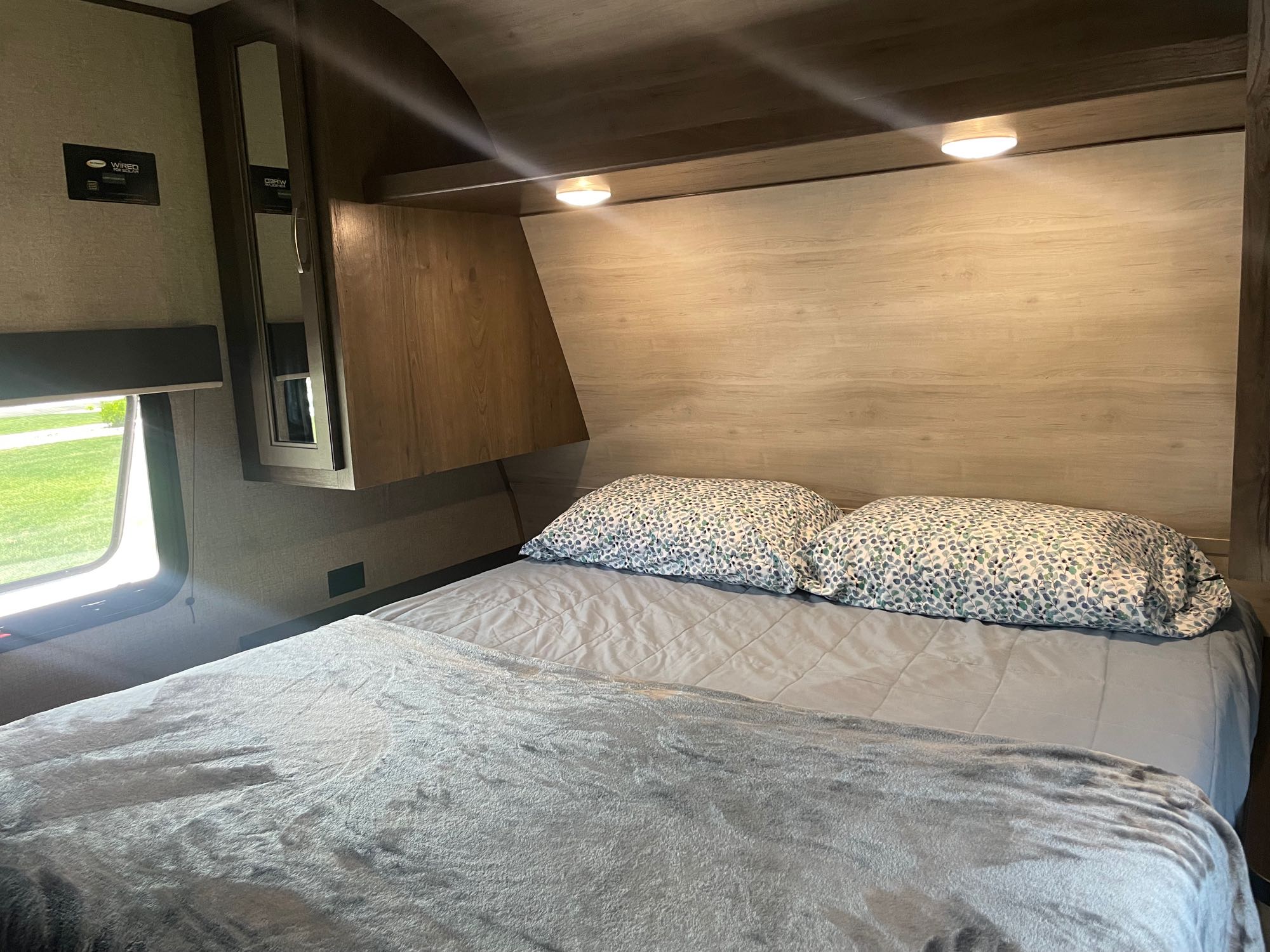 Clean and cozy RV rental bedroom. Features a comfy bed, patterned pillows, built-in lights, and a window.. Jayco Jay Flight SLX 2021