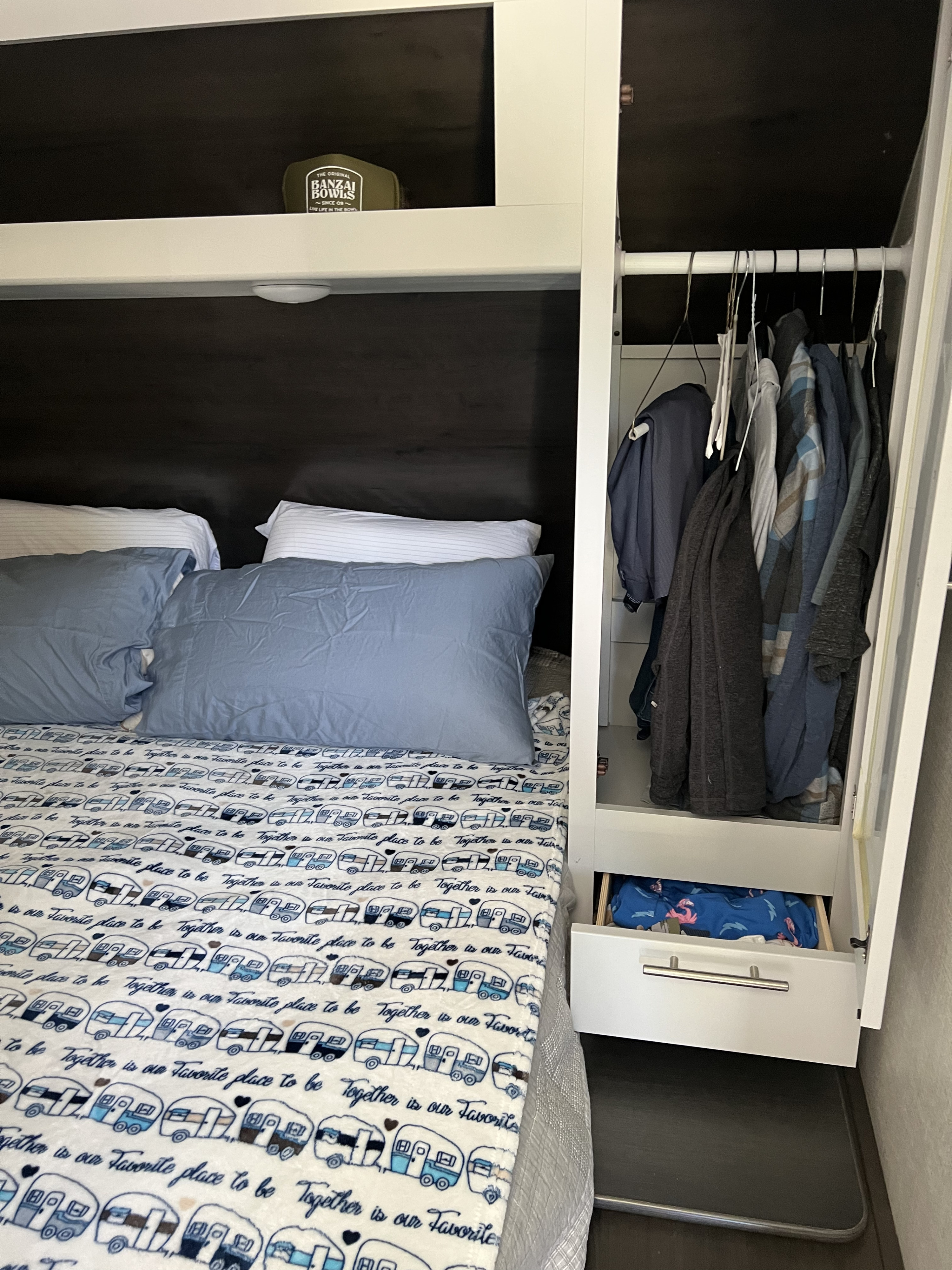 Cozy rv rental bedroom showing a bed with camper-patterned blanket, compact hanging closet, and drawer storage.. Keystone RV Bullet Ultra Lite 2020