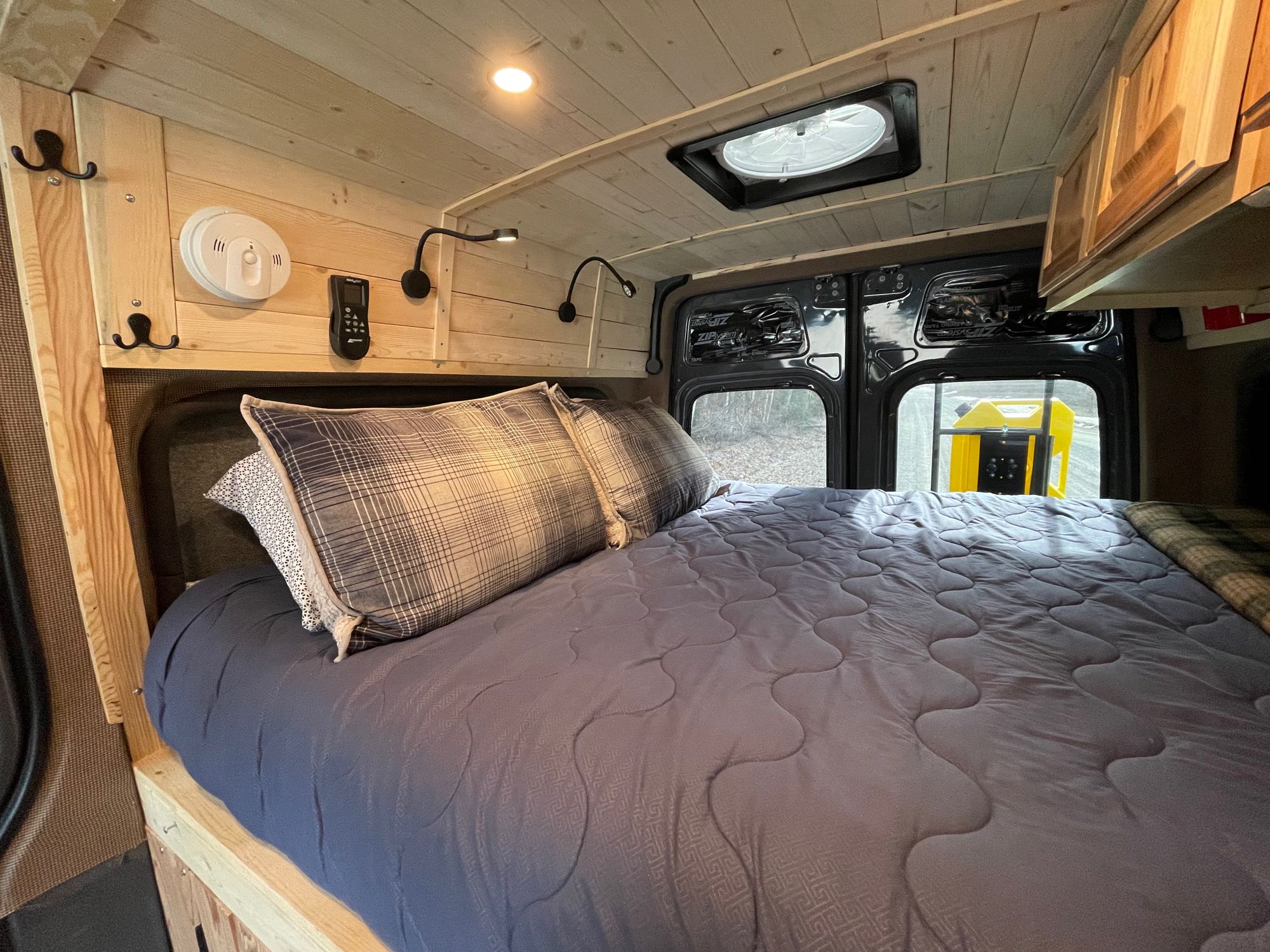 Comfortable RV rental bed in a wooden camper van interior. Features include reading lights, ceiling vent, and CO detector.. Mercedes Sprinter 2022