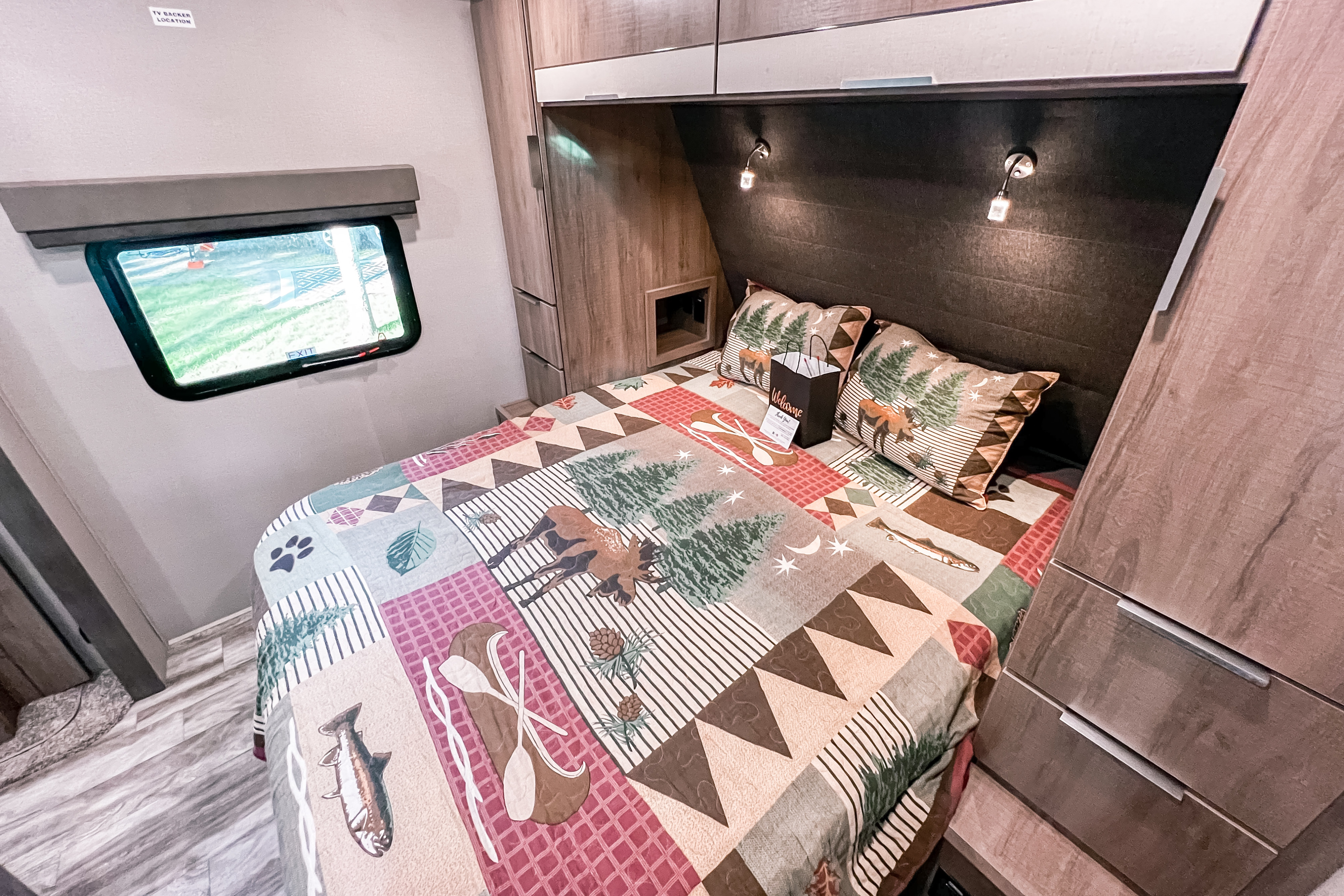 Explore comfort in this RV rental bedroom featuring a rustic nature-themed quilt, cozy reading lights, and ample storage.. Grand Design Reflection 2021