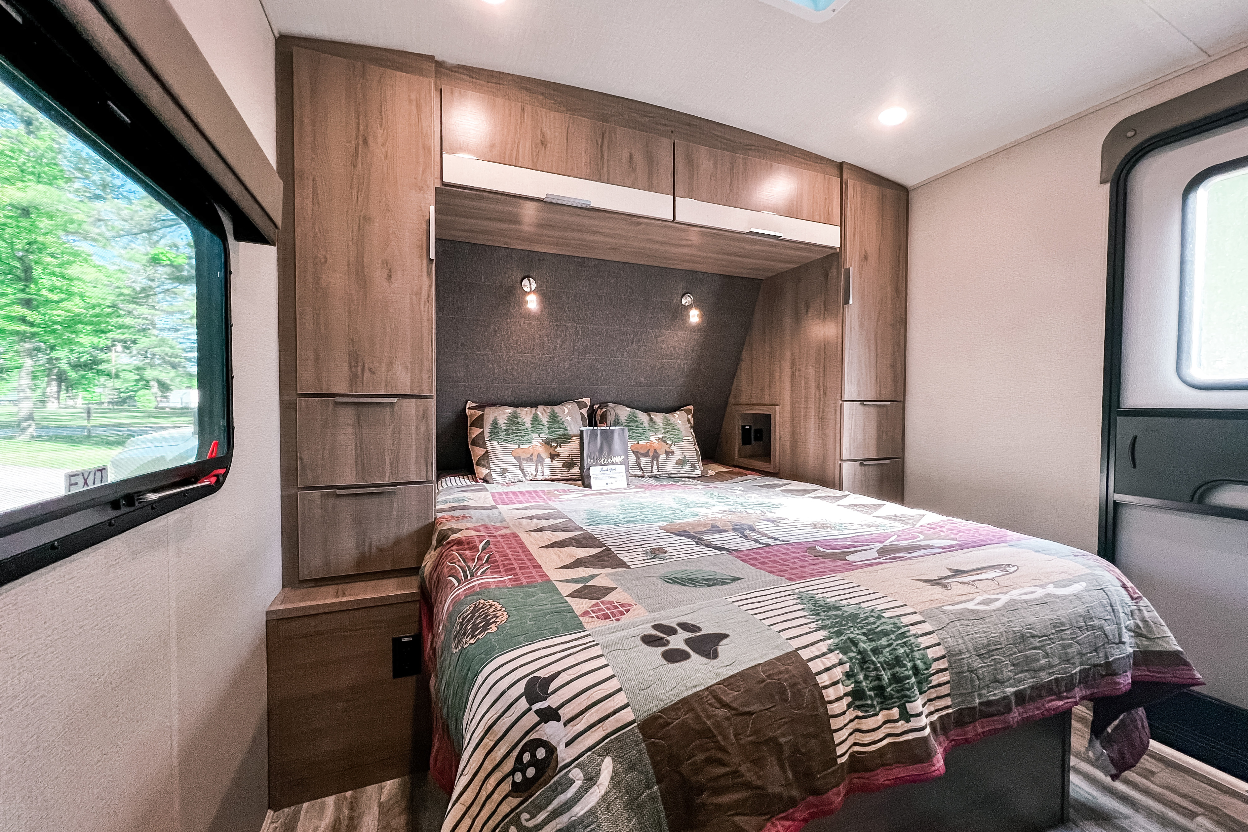 Inside a cozy rv rental, this bedroom offers a comfy bed with nature-themed bedding, storage, and a window view.. Grand Design Reflection 2021