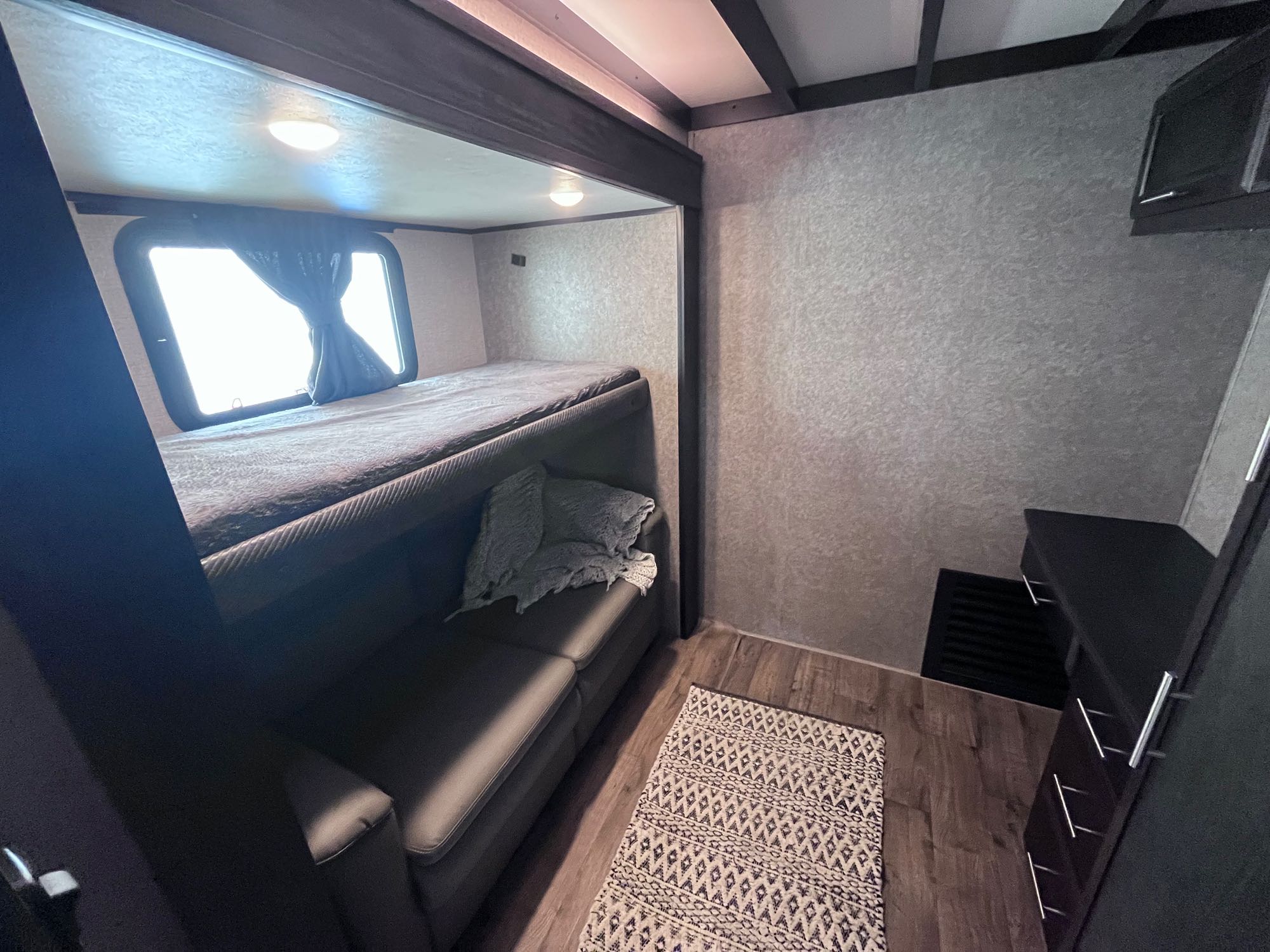 RV rental bunk room featuring an upper bed, lower sofa, storage, and rug. A practical & cozy interior space.. Jayco Eagle 2021