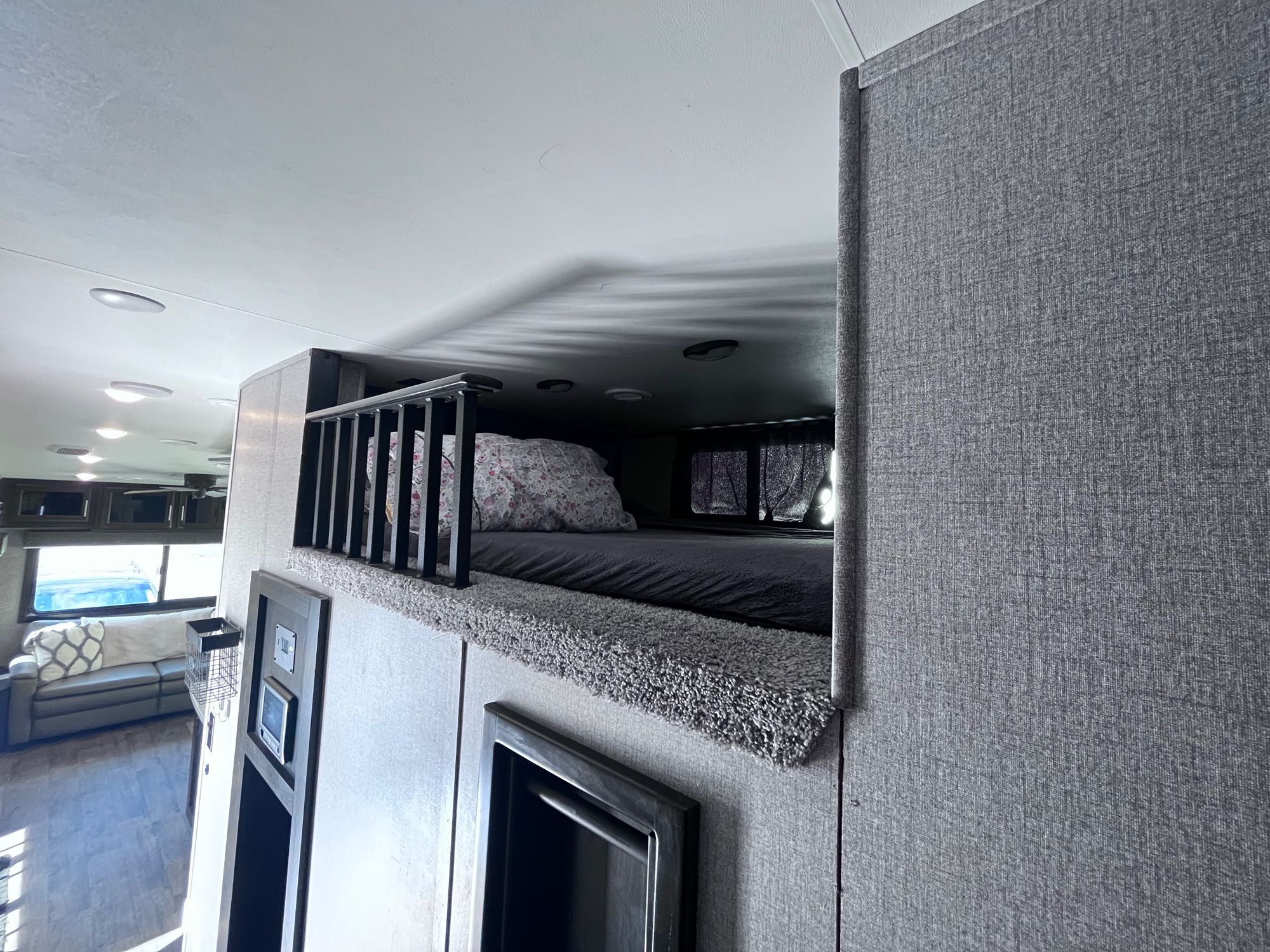 Modern RV rental interior: cozy upper bunk bed overlooks a comfortable living area, detailed with gray textures.. Jayco Eagle 2021
