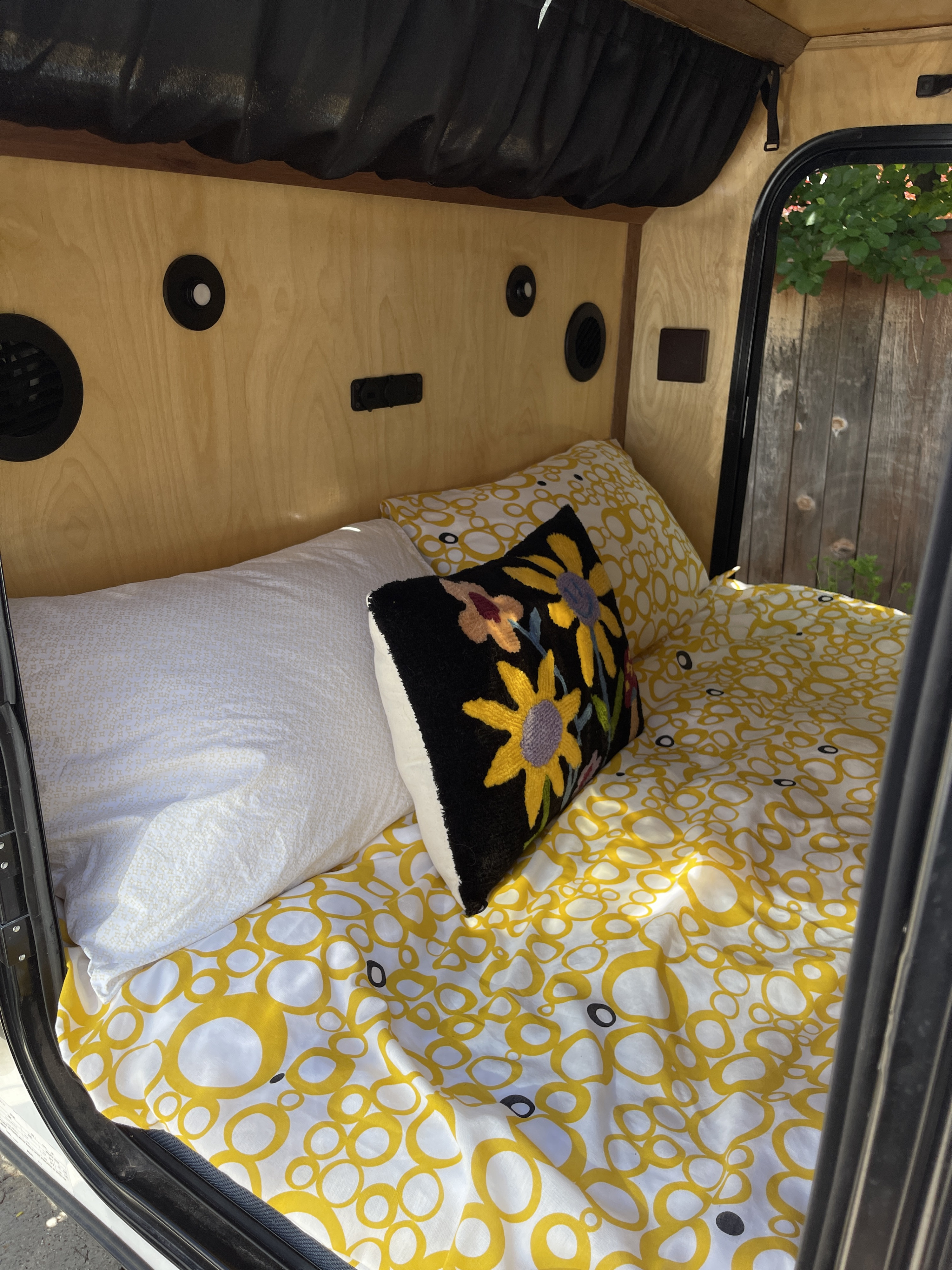 Compact rv rental sleeping area featuring yellow patterned bedding, a colorful floral pillow, and warm wood paneling.. Vintage Trailer Works XTR Other 2023