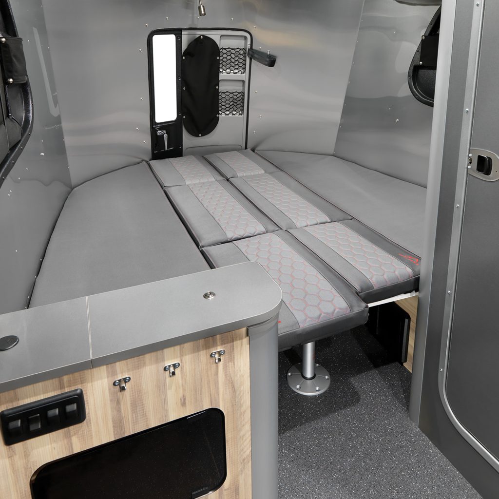 A modern RV rental interior features a versatile living space with a large gray convertible bed and sleek metallic walls.. Airstream Basecamp 2020