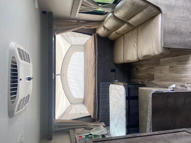 Inside an rv rental: bed in a pop-out section, tan sofa, wood-look interior, and wall-mounted AC unit.. K-Z Manufacturing Other 2019