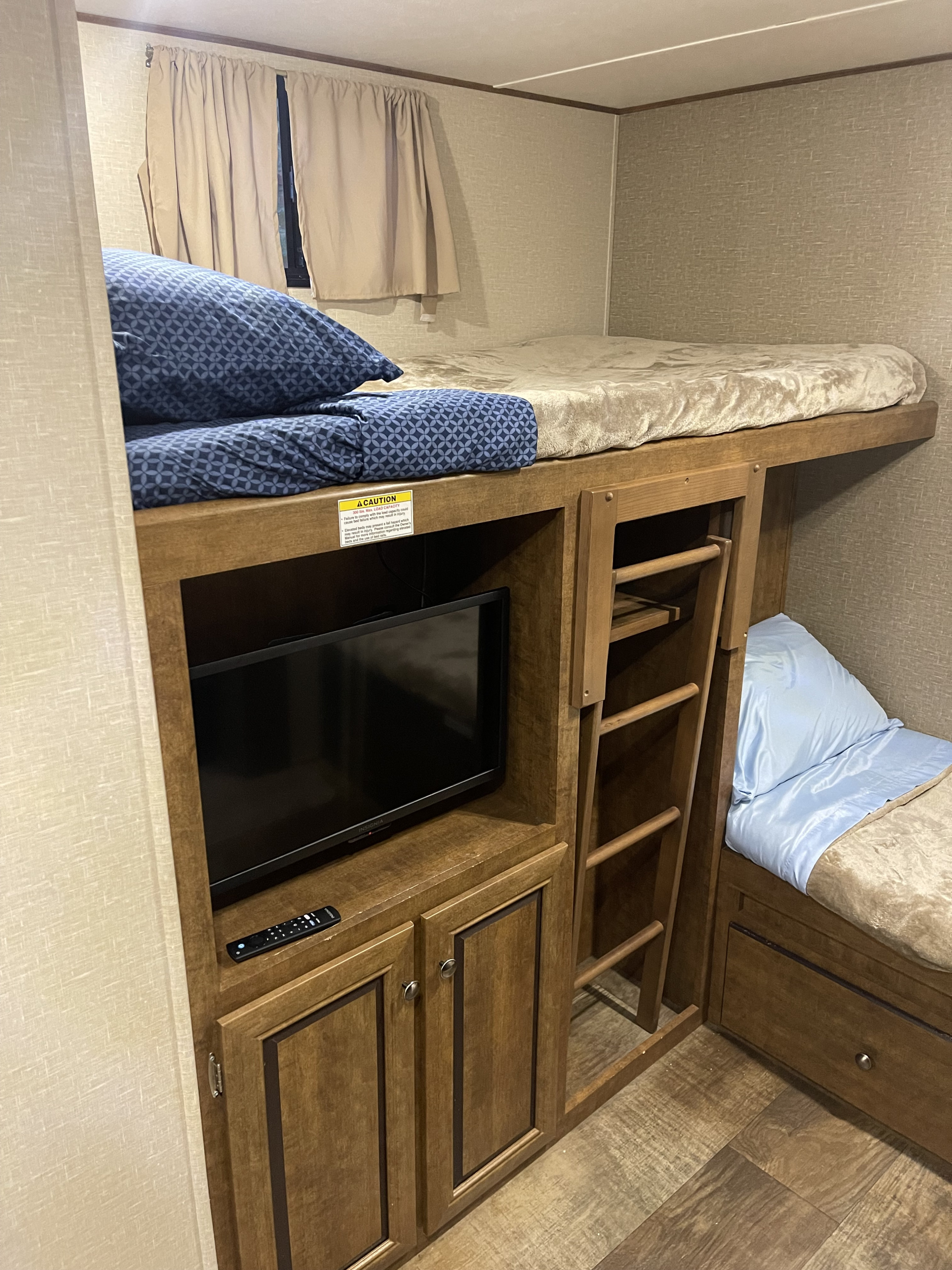 Inside an RV rental: a compact sleeping area with upper and lower bunk beds, TV, storage, and a ladder.. Crossroads RV Z-1 2016
