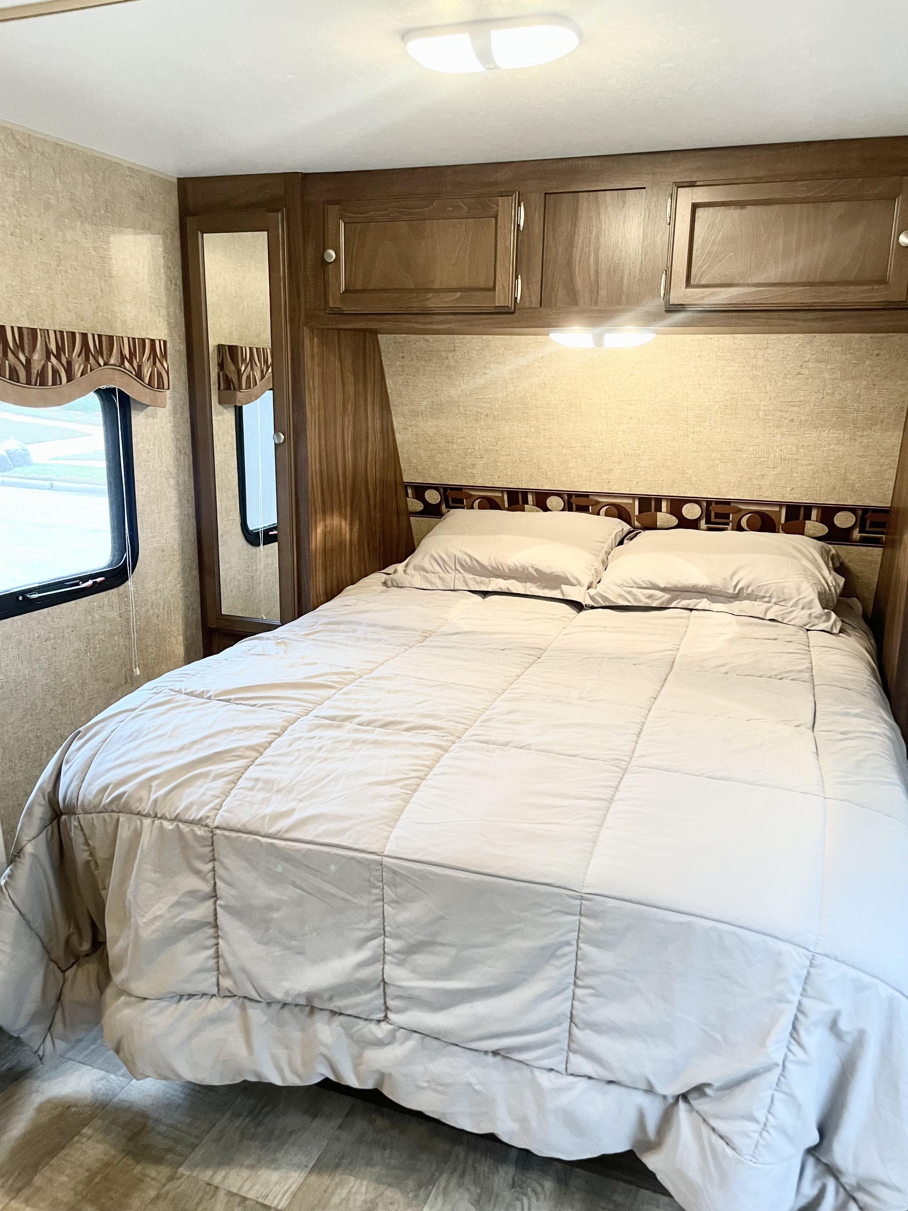 Inviting RV rental bedroom with a comfortable bed, overhead cabinets, mirrored closet, and window. Ready for your trip!. Sportsmen Show Stopper 2016