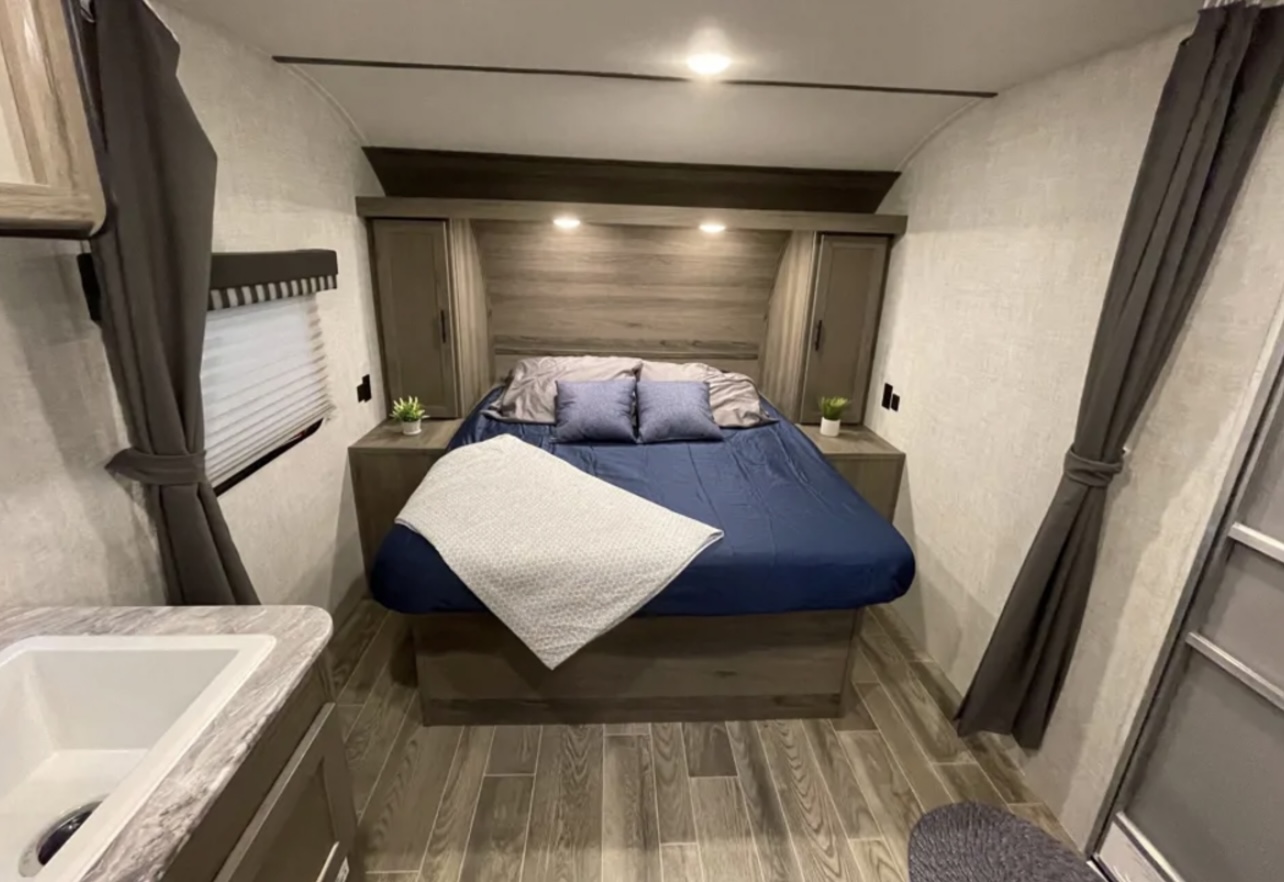 Inviting RV rental bedroom with comfortable bed, built-in storage, and convenient sink area. Perfect for travel.. Grandriver 25BH 2021