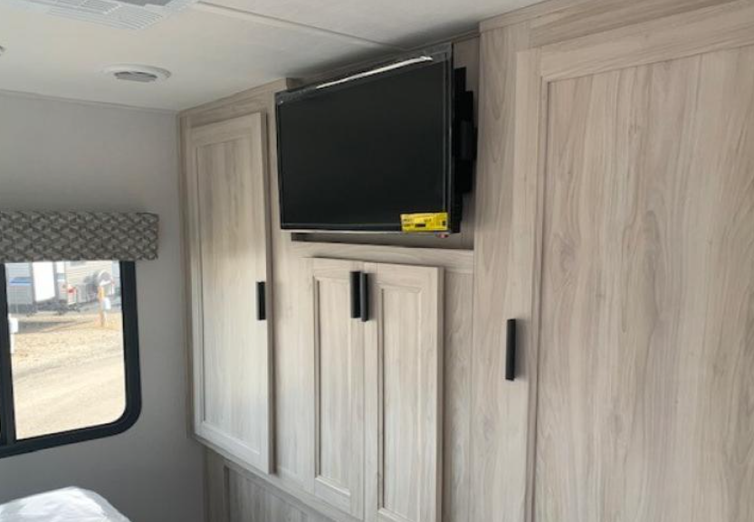 This RV rental bedroom features a mounted TV above light wood cabinetry, offering ample storage and a window view.. Forester Classic 2023