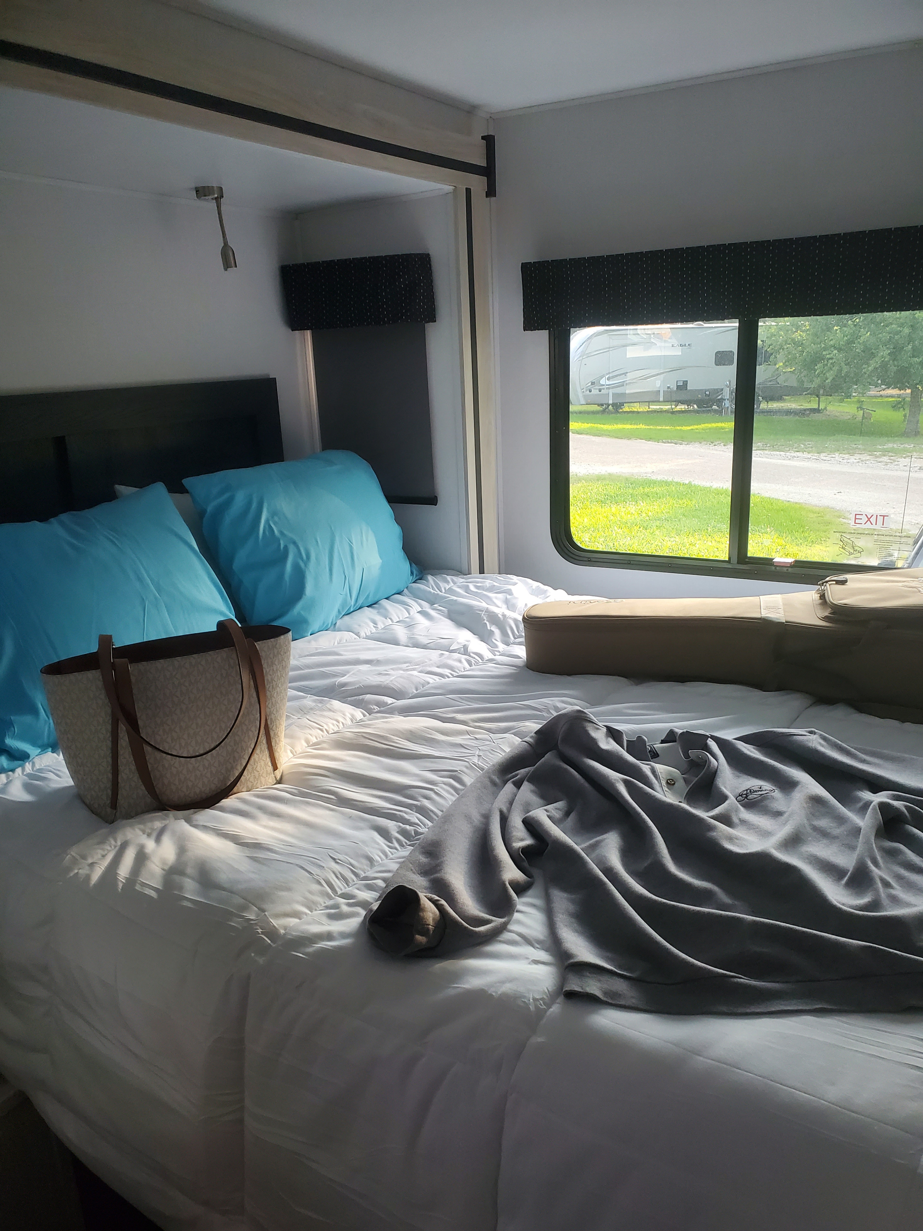 Cozy RV rental bedroom with a bed, blue pillows, and a view of another RV at a campsite. Ideal for comfortable travel.. Forester Classic 2023