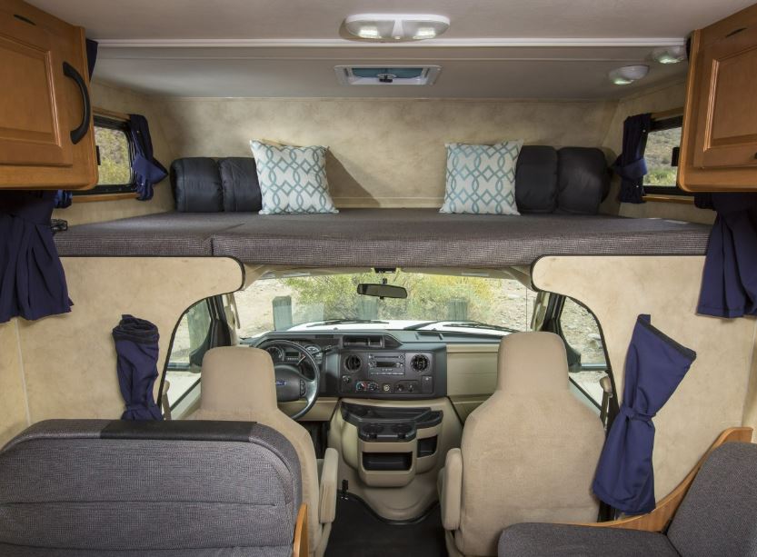 RV rental interior: view from the living area showing the over-cab bunk bed, front cab, and beige seating.. Thor Majestic 2018