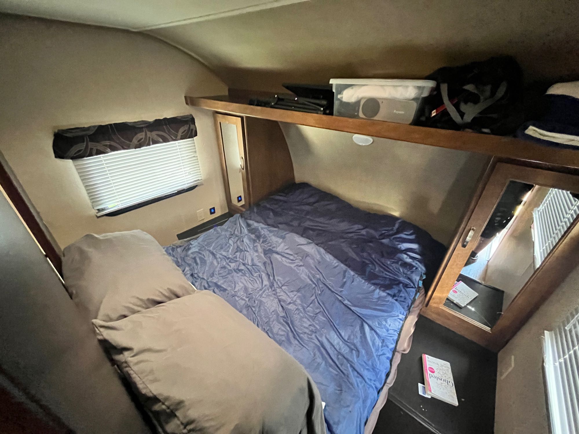 Inside an RV rental, a compact bedroom features a bed with blue linens, pillows, a window, and overhead storage.. Forest River Salem Cruise Lite 2017