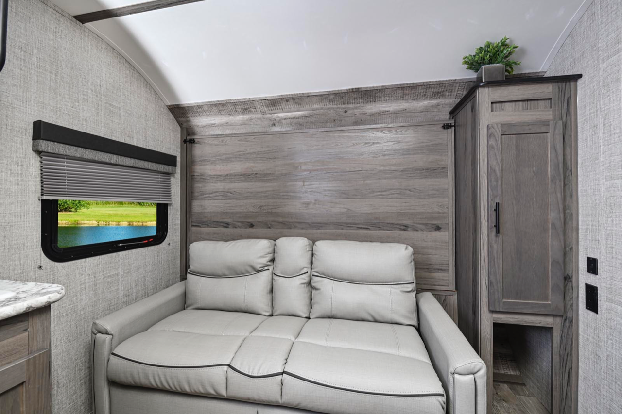 Spacious RV rental interior featuring a light gray sofa, window with lake view, and distressed wood-look wall accents.. Gulf Stream Ameri-Lite Super Lite 2022