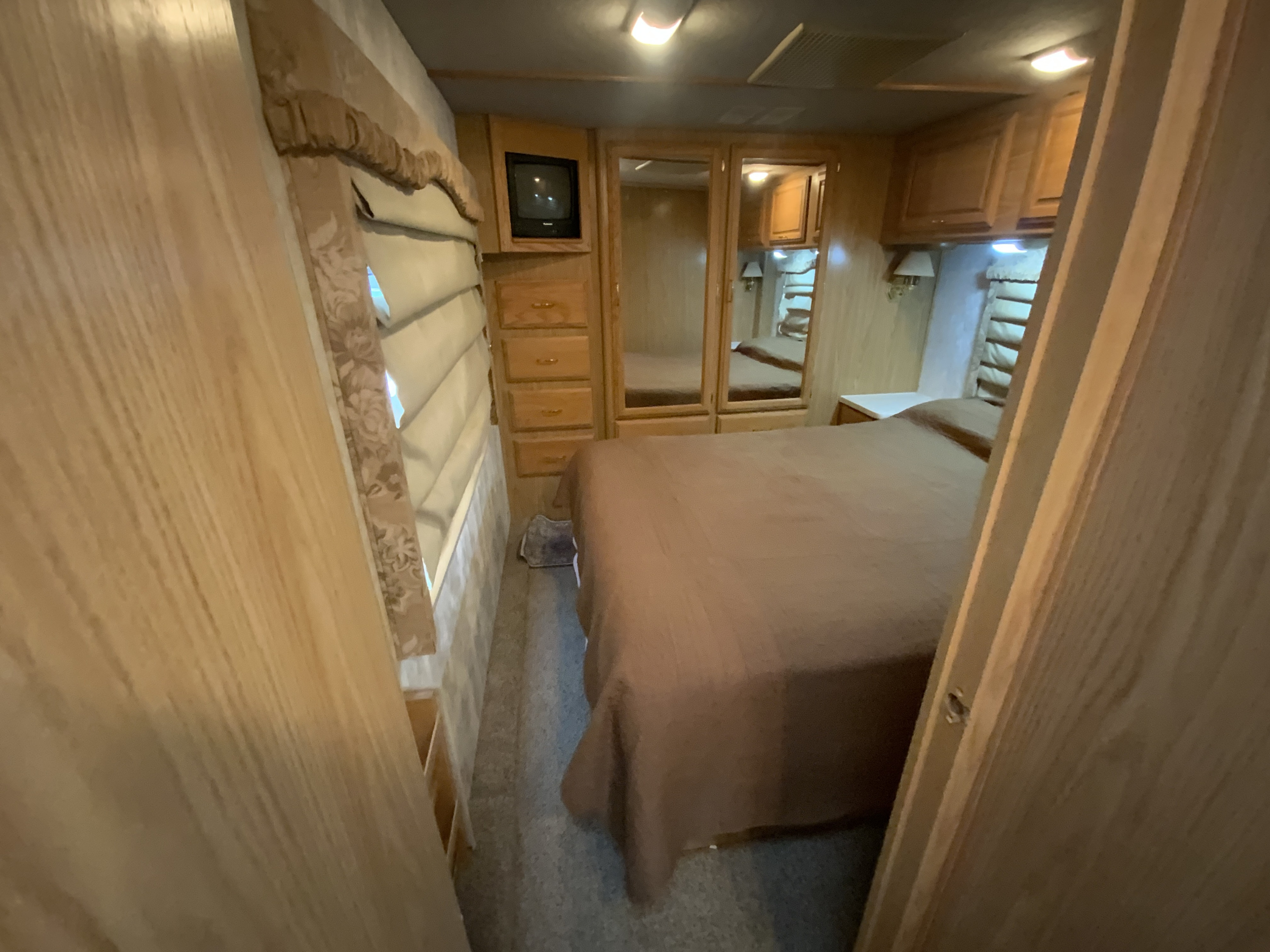 Inside an RV rental, a compact bedroom with a bed, wood dresser, and mirrored closet doors.. Fleetwood Bounder 2000