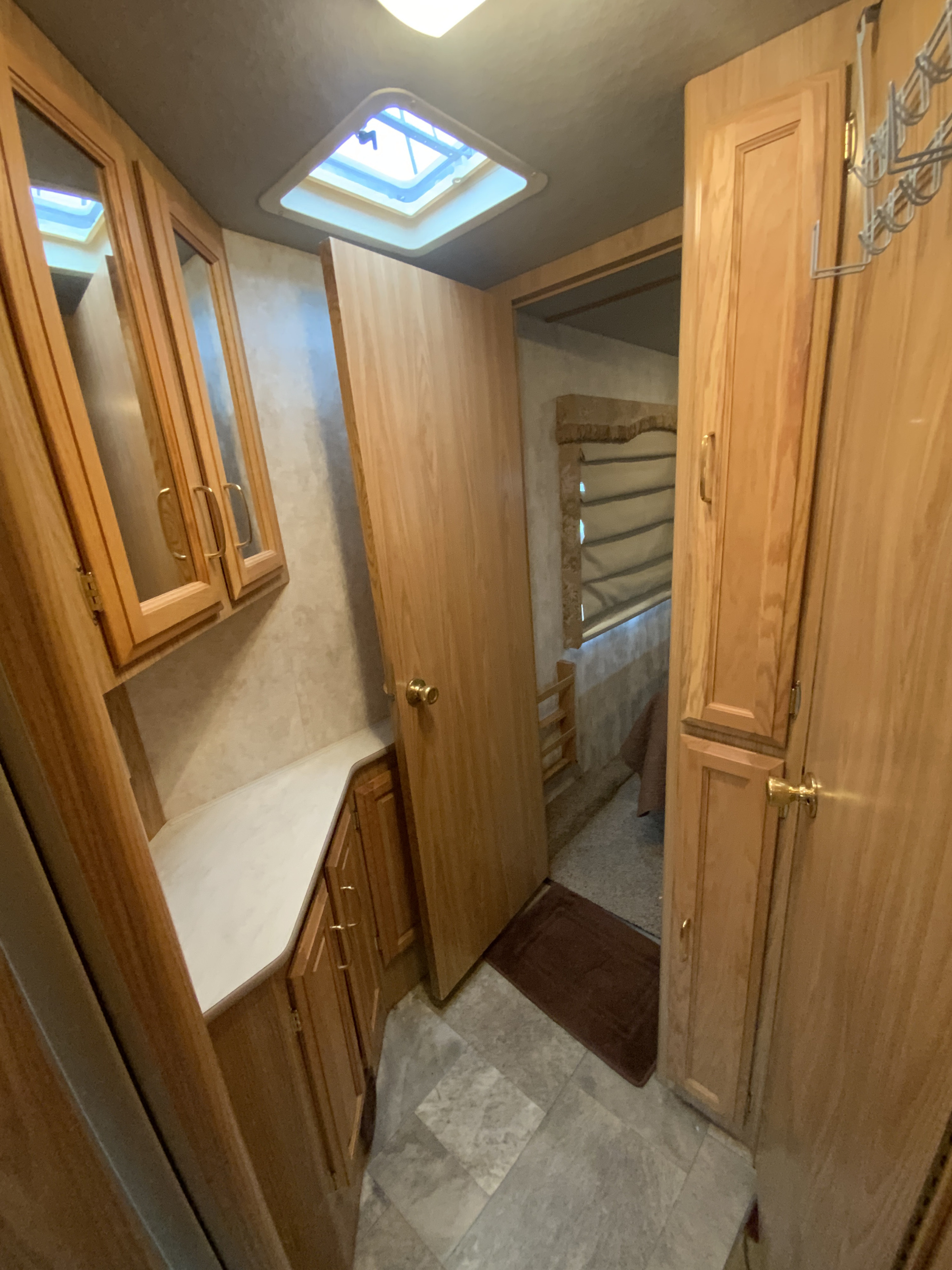 Bright RV rental interior: light wood cabinetry, white counter, tiled floor, skylight, and open door to bedroom.. Fleetwood Bounder 2000