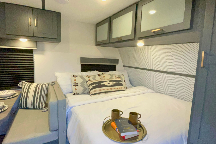 RV rental bedroom features a cozy bed with patterned pillows, smart overhead cabinets, and a compact dining nook.. Keystone RV Bullet Crossfire 2022