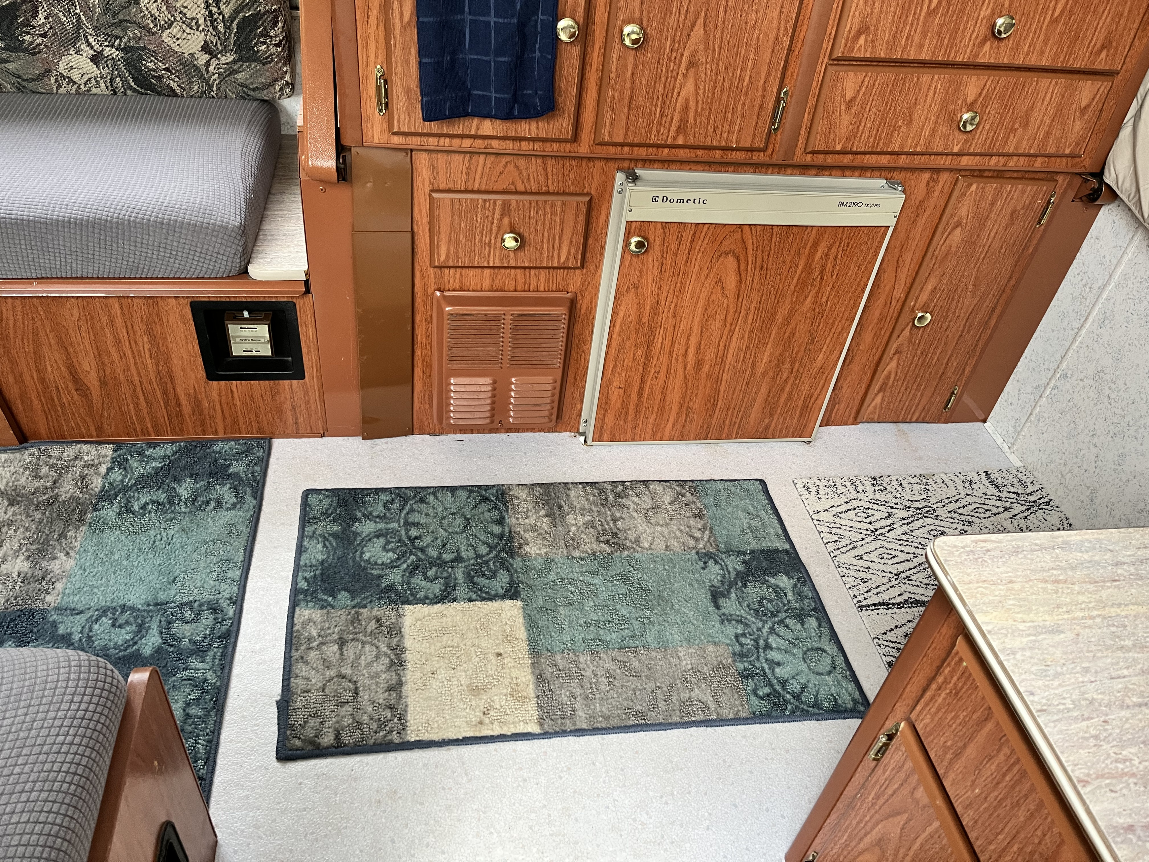 Warm wood interior of an rv rental features a Dometic fridge, comfy bed with grey cover, and patterned rugs.. Coleman Americana Utah 1995