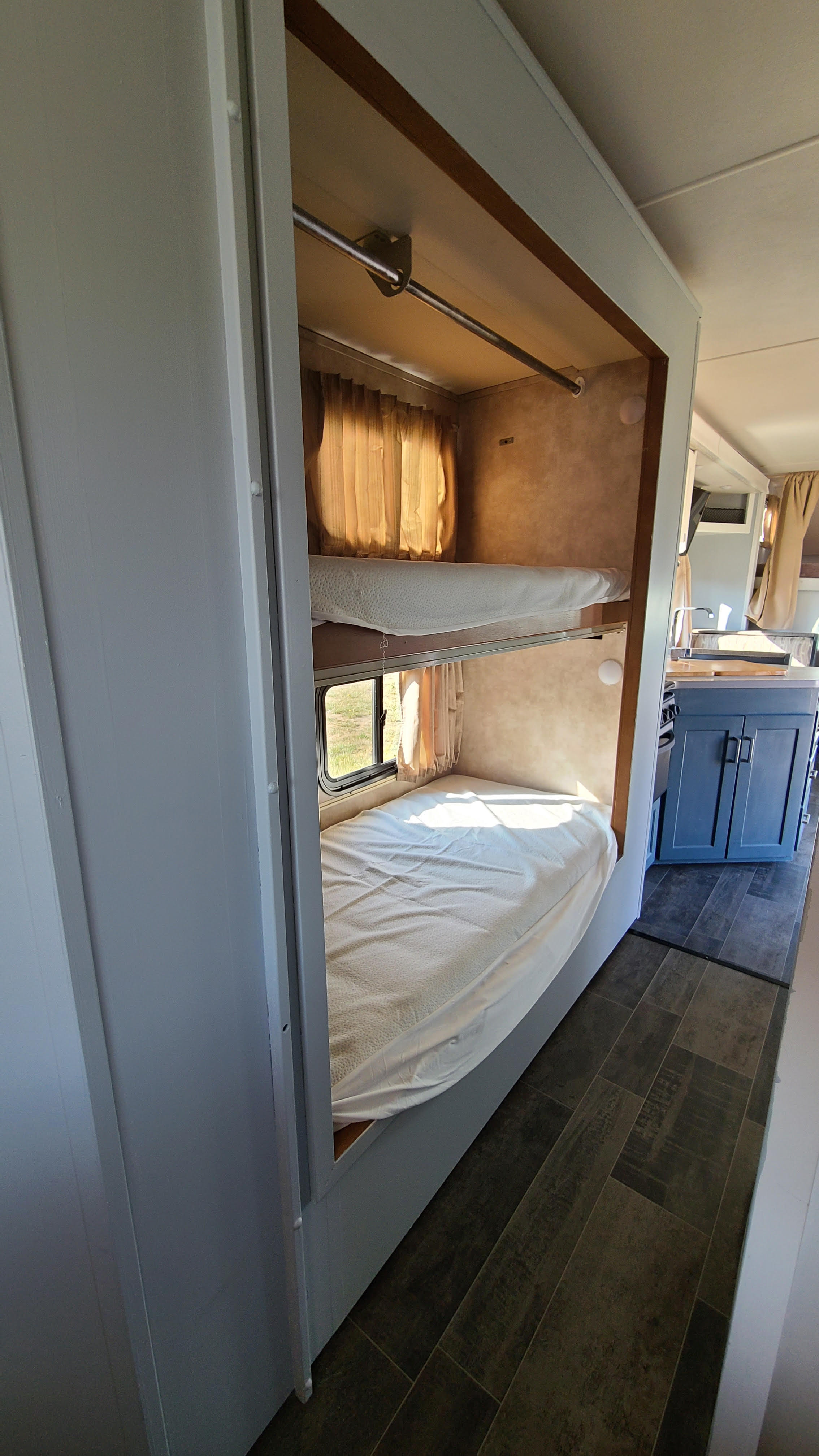 Inside this RV rental, cozy bunk beds with white sheets offer sleeping space, with a partial view of the modern kitchen.. Winnebago Minnie Winnie 2019