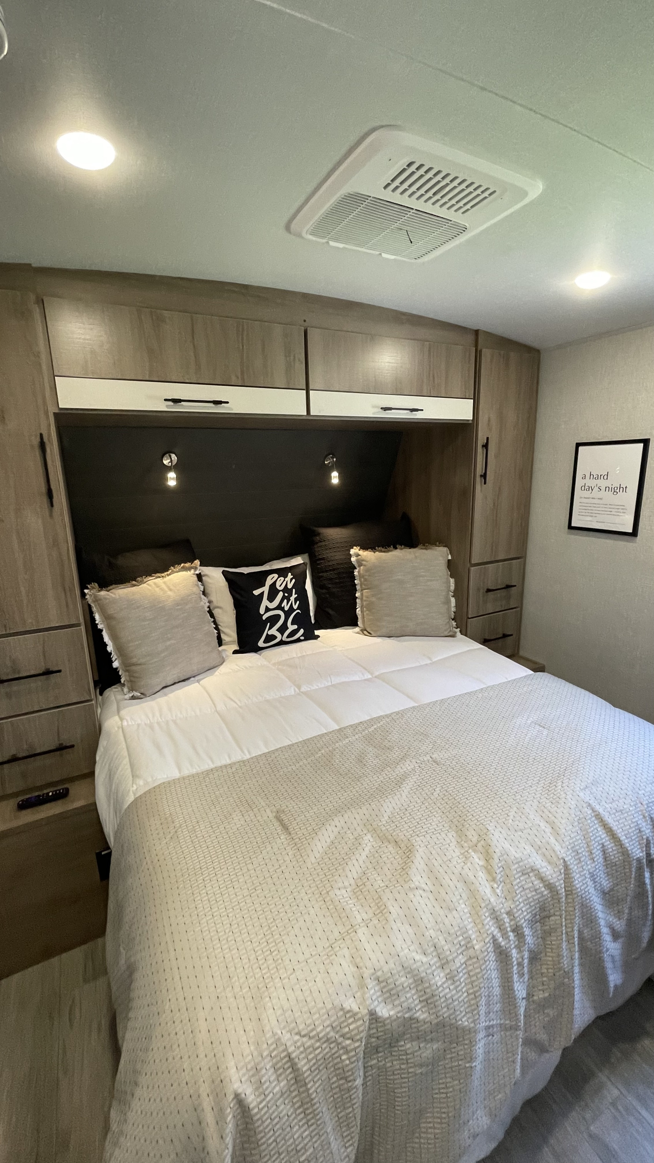 Cozy RV rental bedroom with ample storage, "Let it BE" pillow, and a "Hard Day's Night" framed art.. Grand Design Imagine 2023