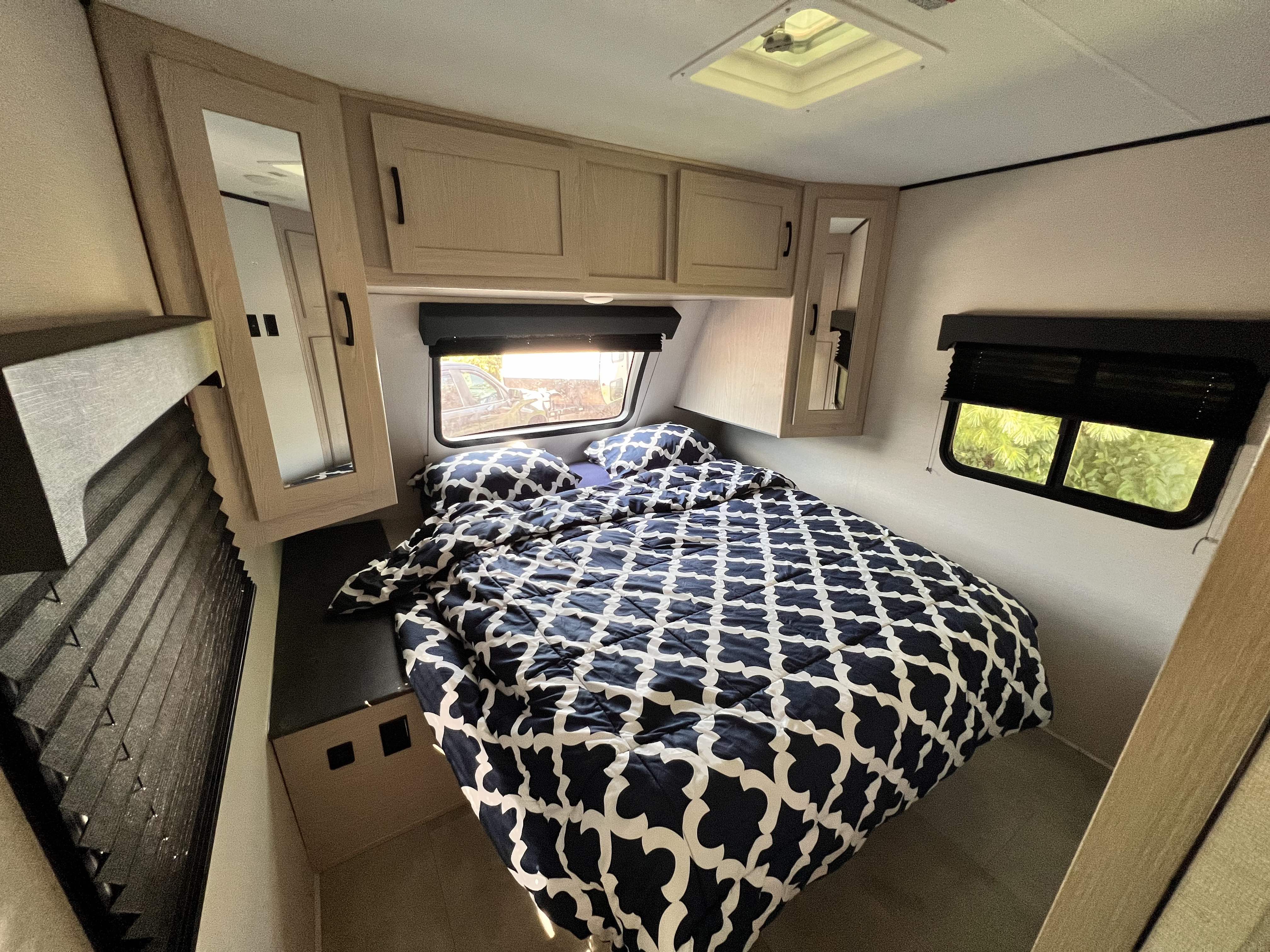 Cozy RV rental bedroom featuring a comfy bed with a patterned comforter, overhead cabinets, and bright windows.. Coachmen Other 2021