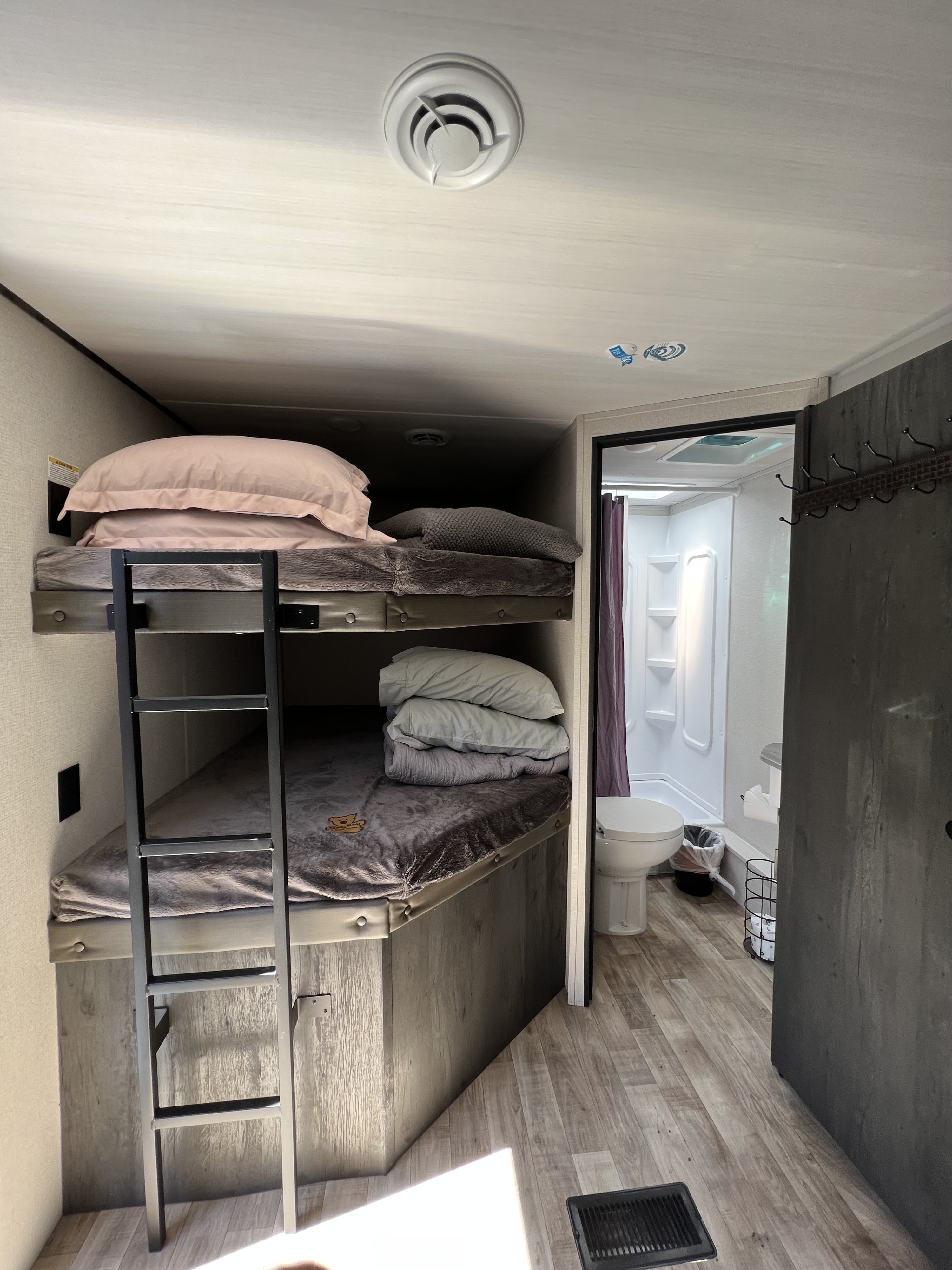 Compact RV rental interior featuring bunk beds with a ladder and a small bathroom with a toilet and shower.. Keystone RV Hideout 2022