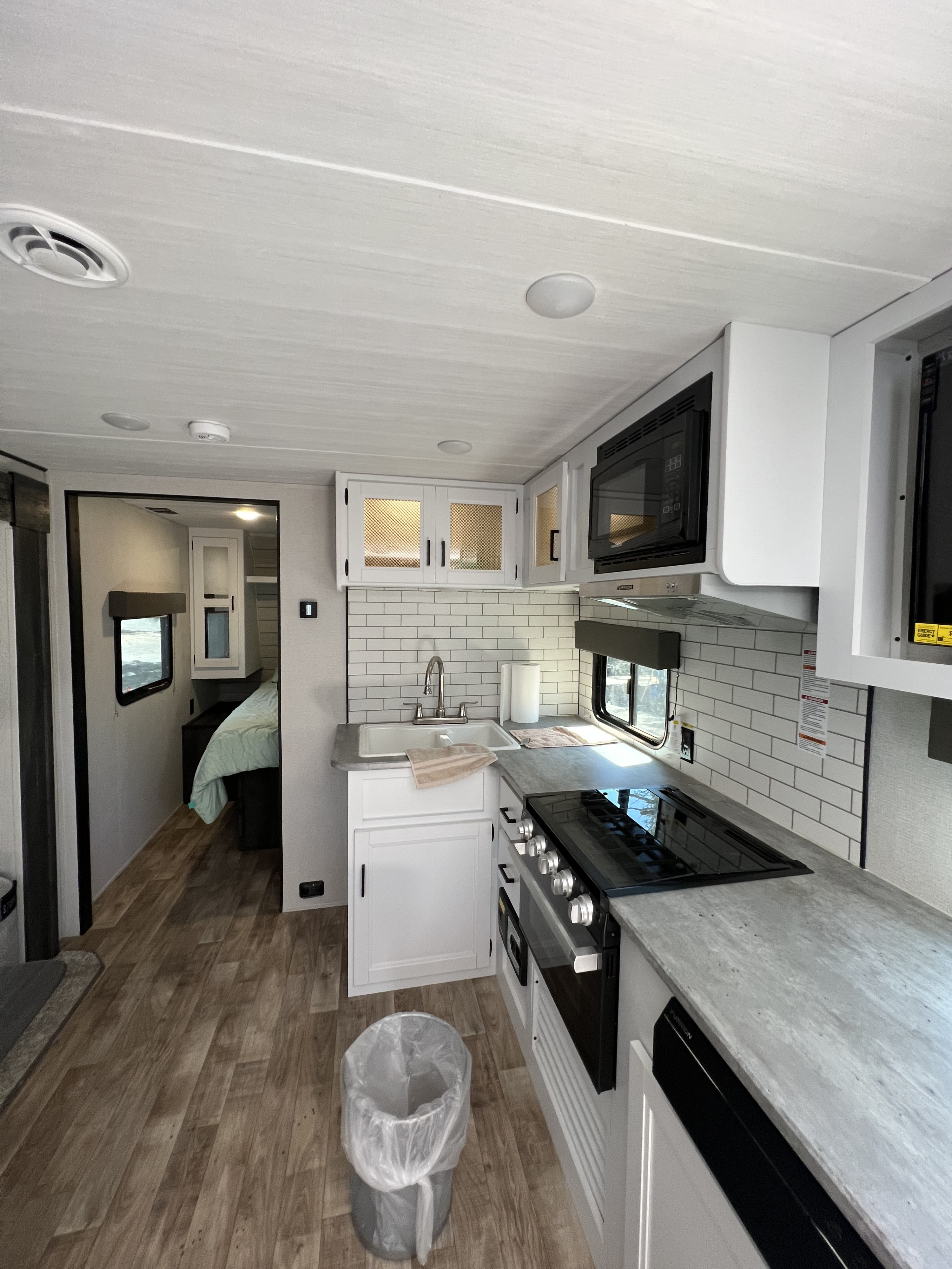 Bright and modern RV rental interior featuring a well-equipped kitchen with a stove, microwave, sink, and an inviting bedroom.. Keystone RV Hideout 2022