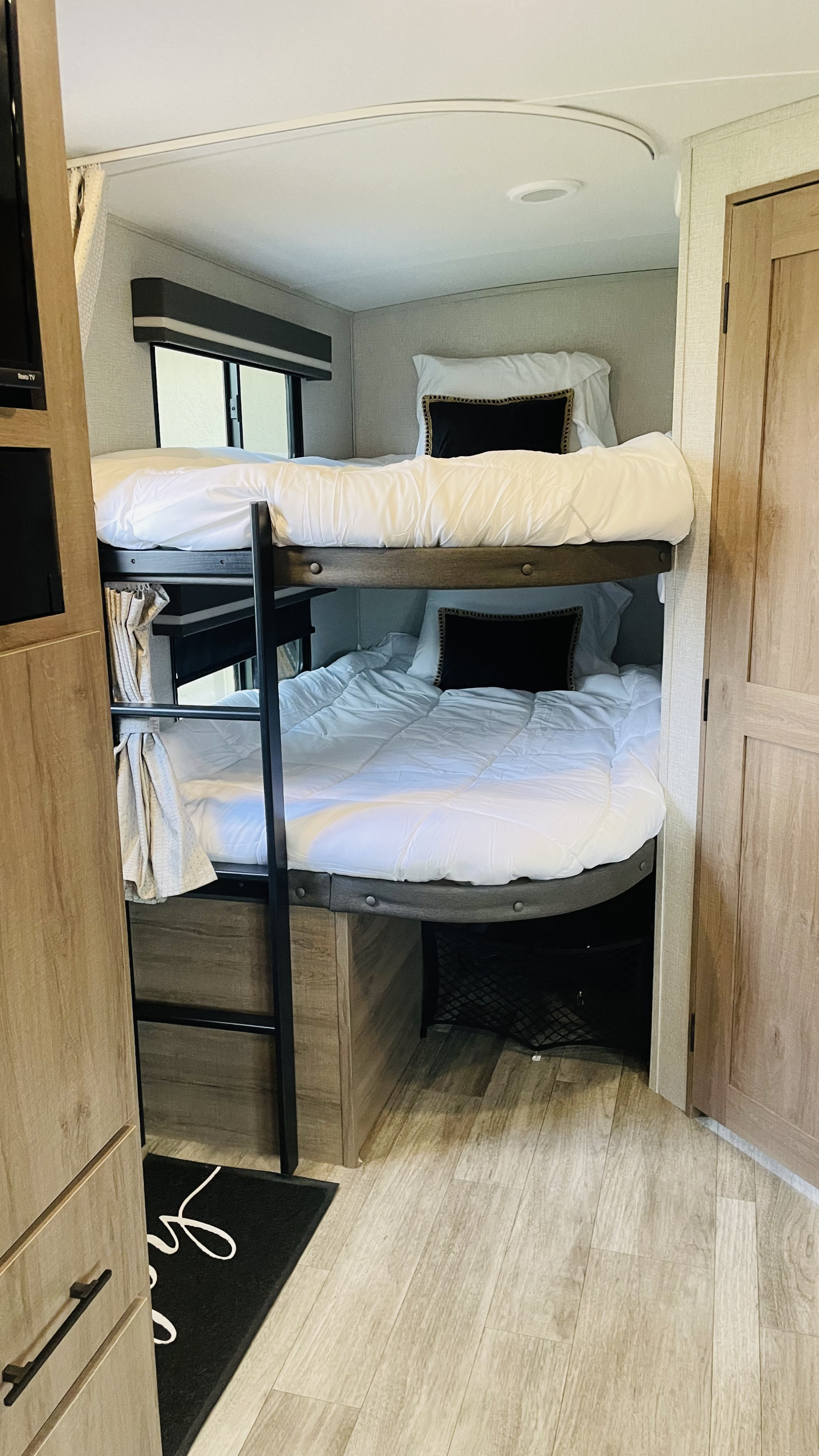 RV rental interior: view of bunk beds with white bedding, black pillows, and wooden cabinetry. Ladder visible for top bunk.. Grand Design Imagine 2023