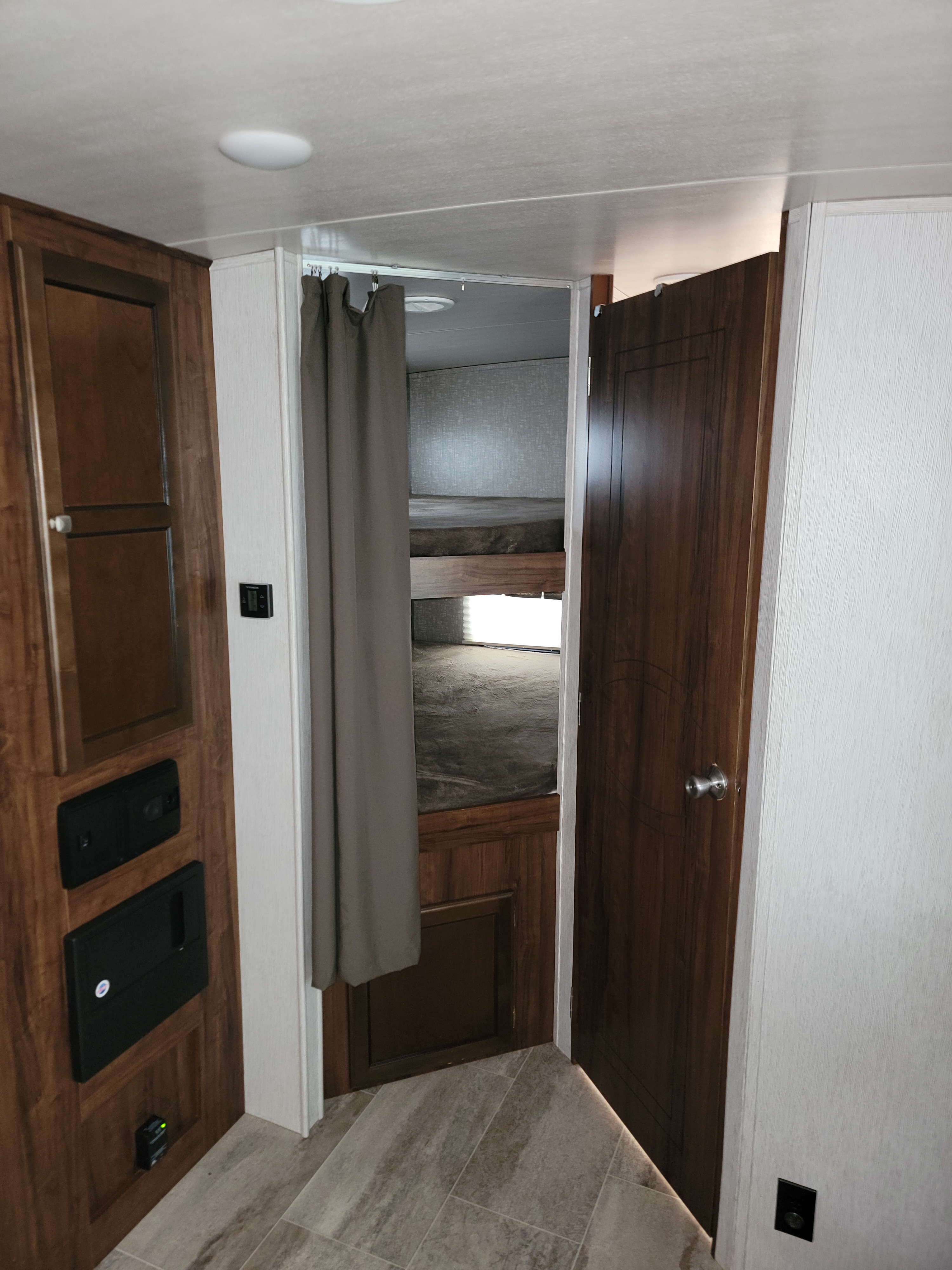 RV rental interior featuring bunk beds, a privacy curtain, wooden cabinetry with controls, and an open door.. Heartland RVs Mallard 2018