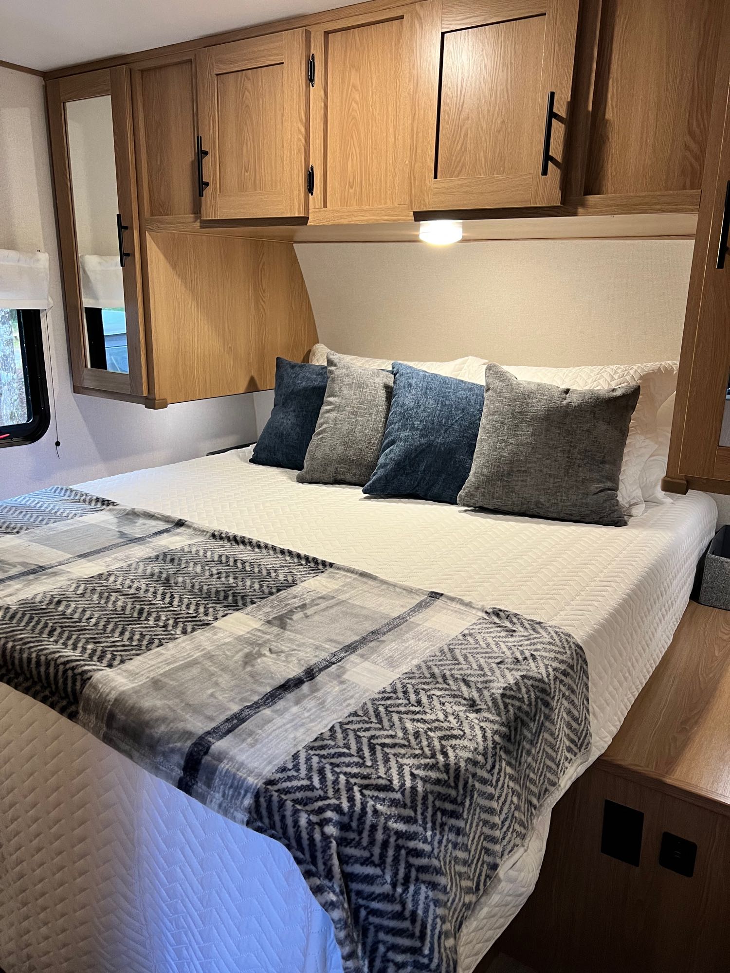 Cozy RV rental bedroom: a comfortable bed with plush pillows and warm wooden cabinets and a light, ready for your next adventure.. Primetime Avenger 26BK Bunkhouse 2023
