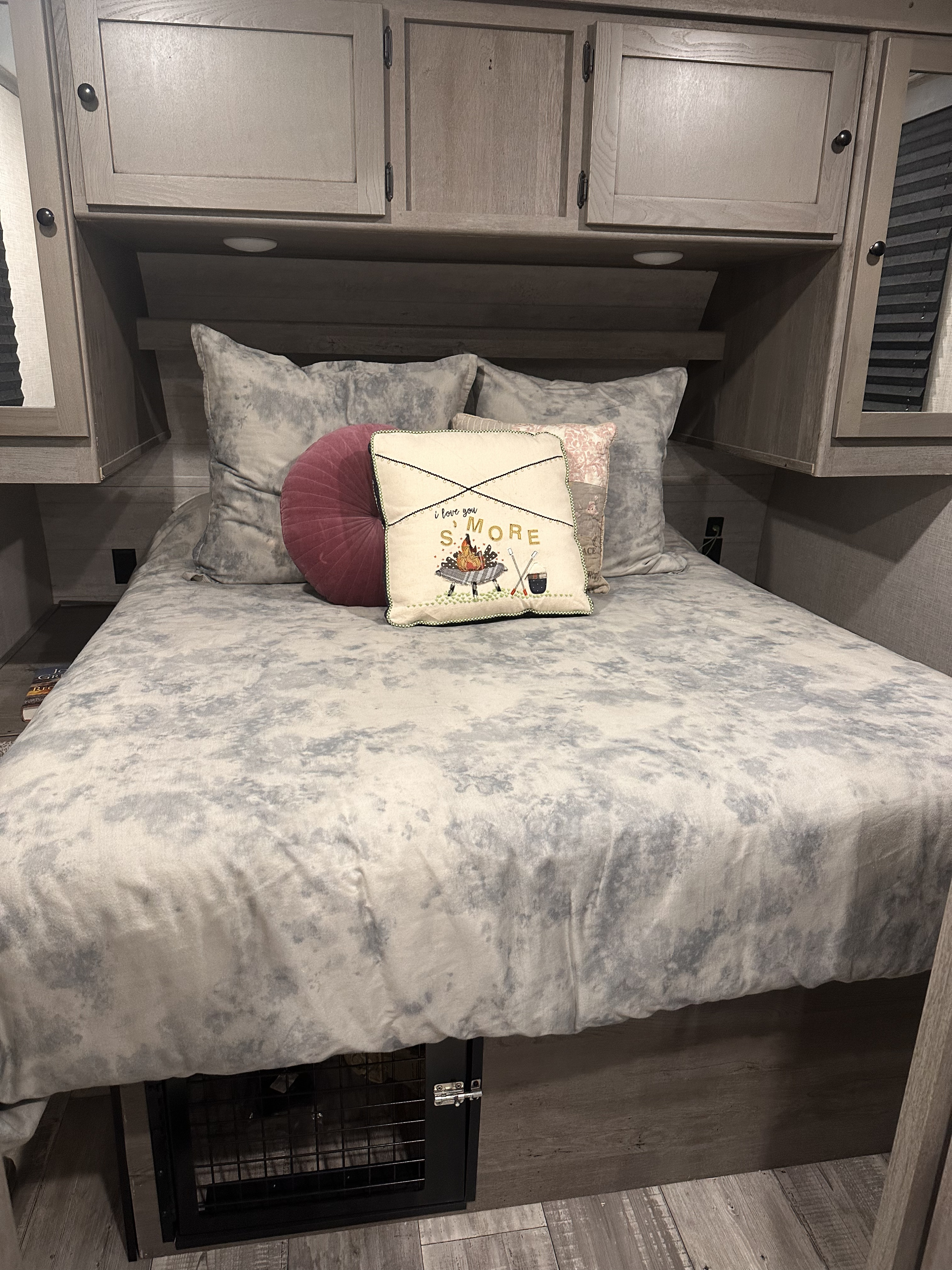 RV rental bedroom: a cozy bed with grey comforter and S'mores pillow, framed by light wood cabinets.. Keystone RV Outback Ultra-Lite 2020
