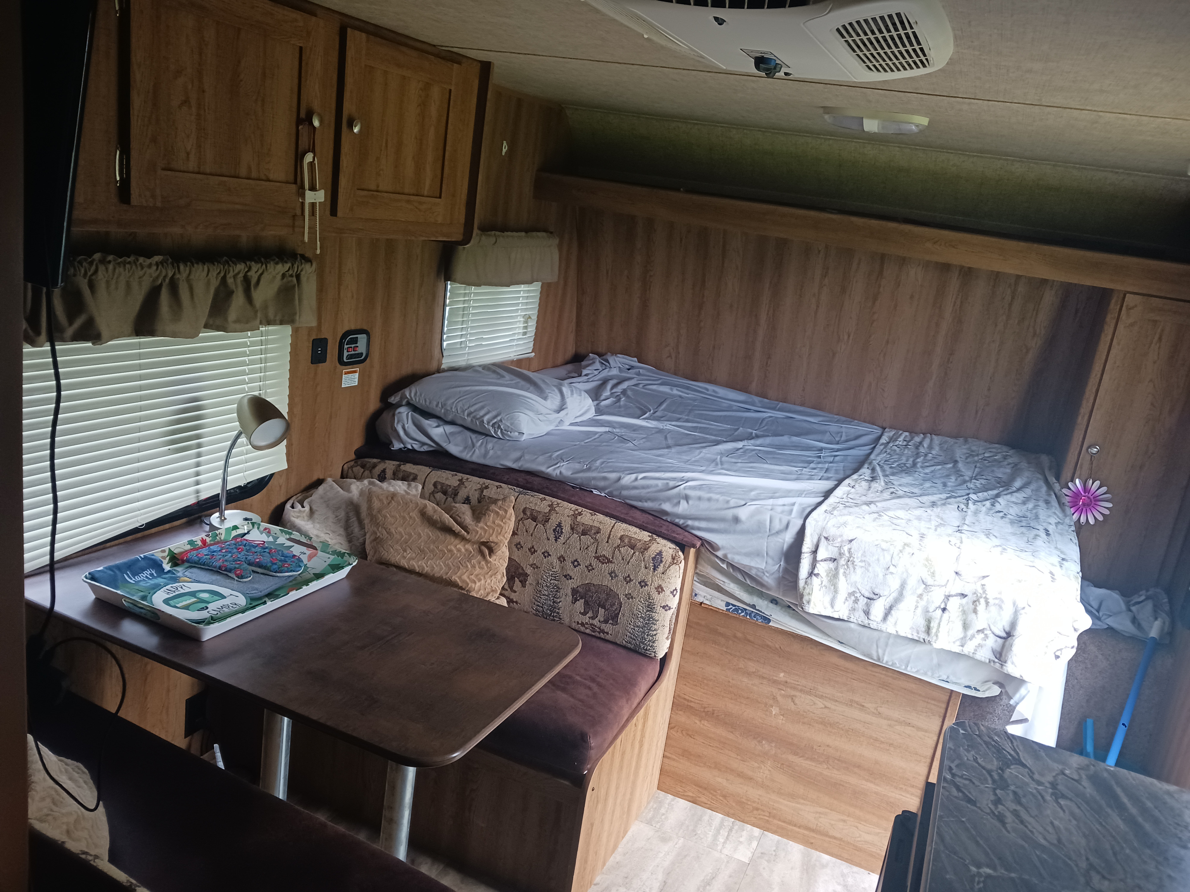 Inside an RV rental: a cozy interior showing a bed, dinette with nature-themed cushions, and wood cabinetry.. Keystone RV Hideout LHS 2016
