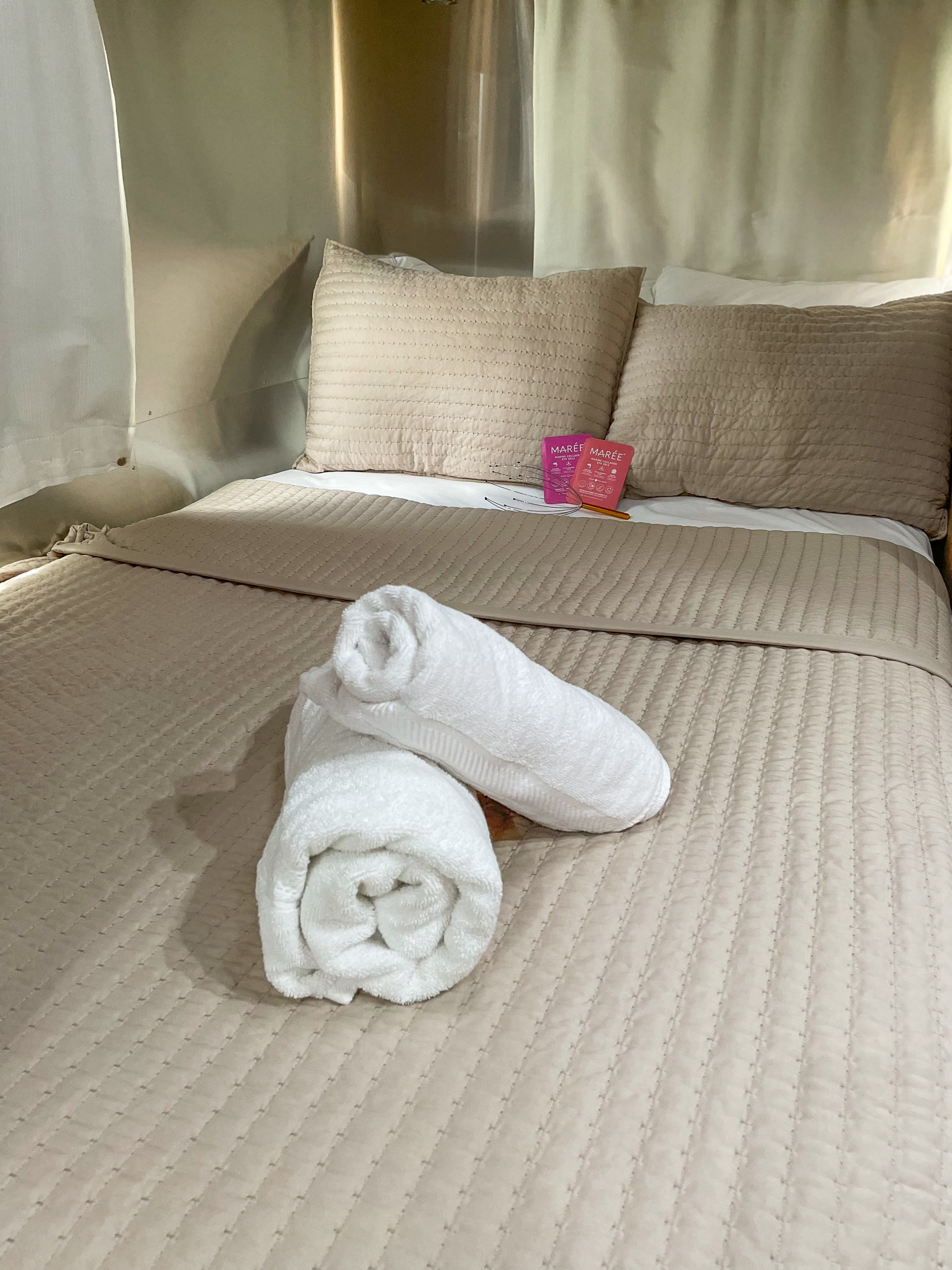 Cozy rv rental bed with beige quilted bedding, soft pillows, and fresh white towels, plus relaxation essentials.. Airstream Flying Cloud 2019