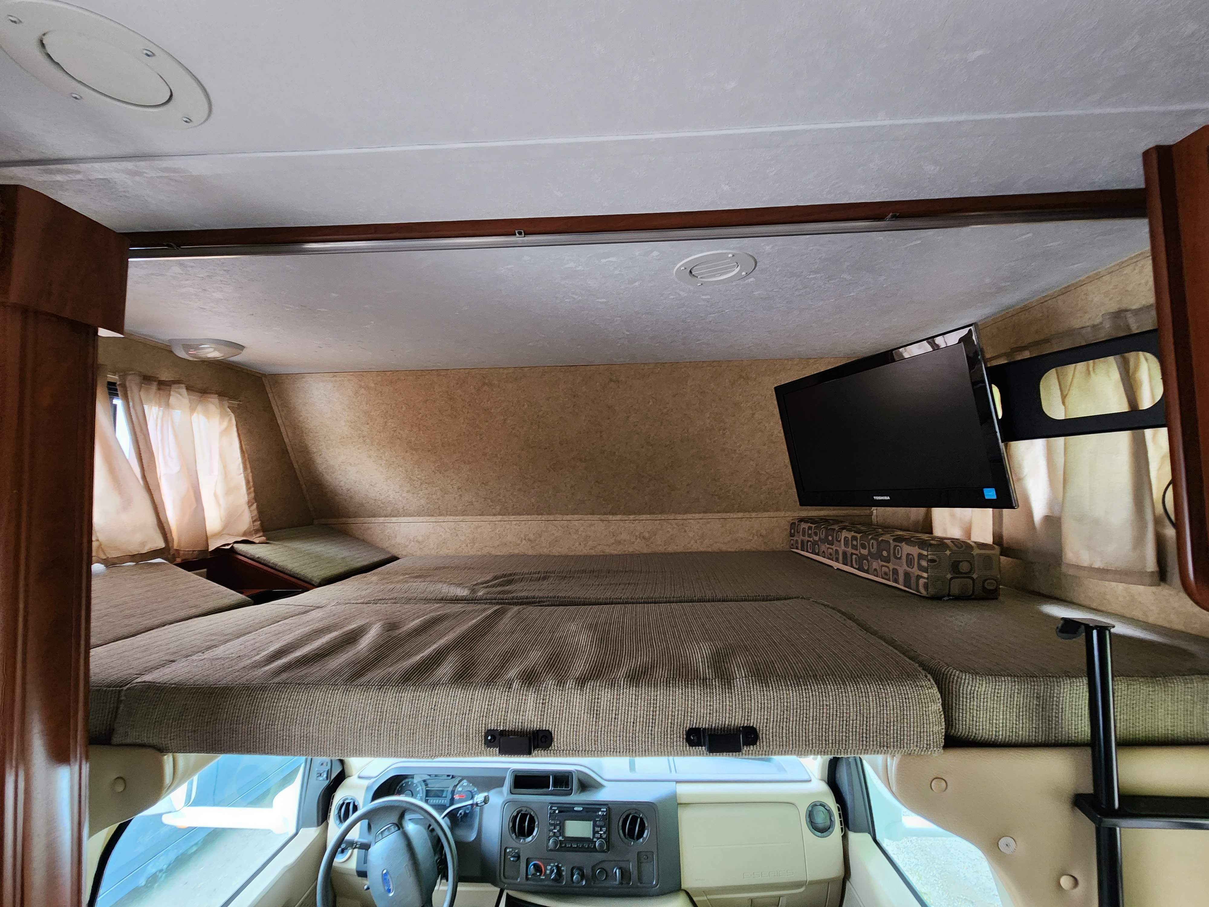 RV rental interior featuring a spacious cab-over bunk bed, mounted TV, and the vehicle's dashboard.. Forest River Sunseeker 2012