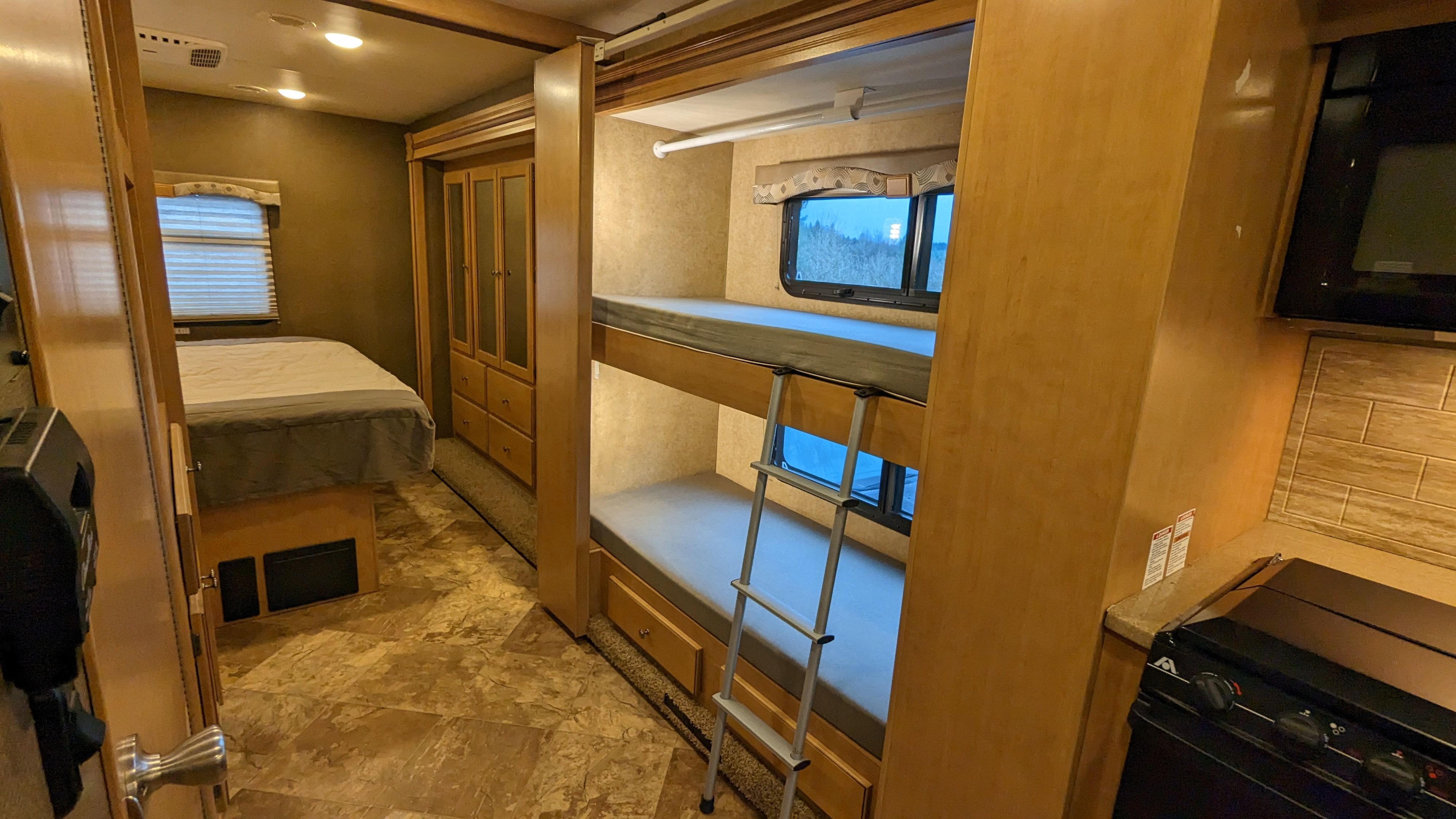 Spacious RV rental interior with bedroom, bunk beds, wardrobe, and kitchen area, perfect for family adventures.. Thor Windsport 2016