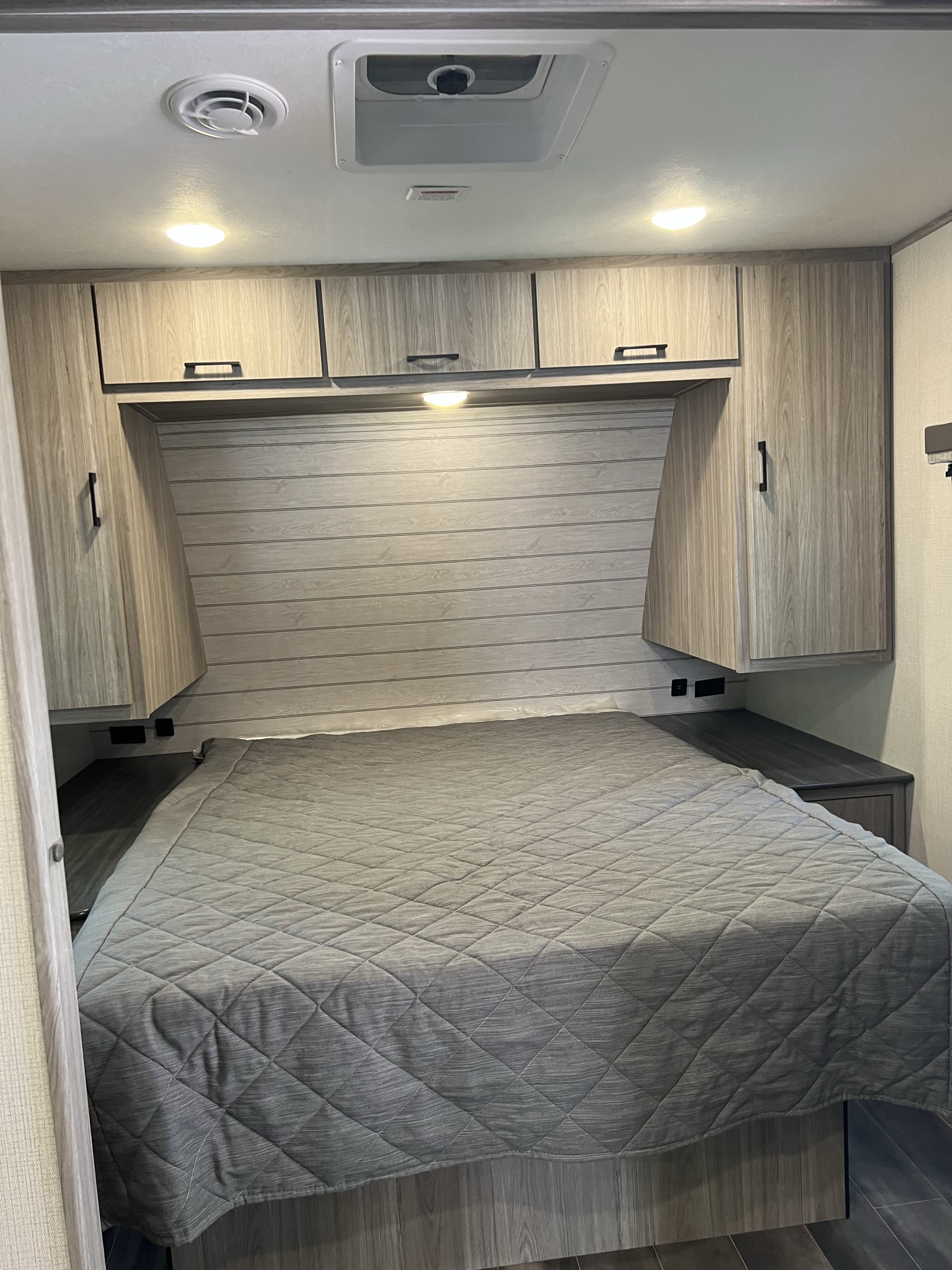 Experience comfort in this RV rental's cozy bedroom, featuring a queen bed, wood-look cabinets, and charging ports.. Keystone RV Passport SL 2021