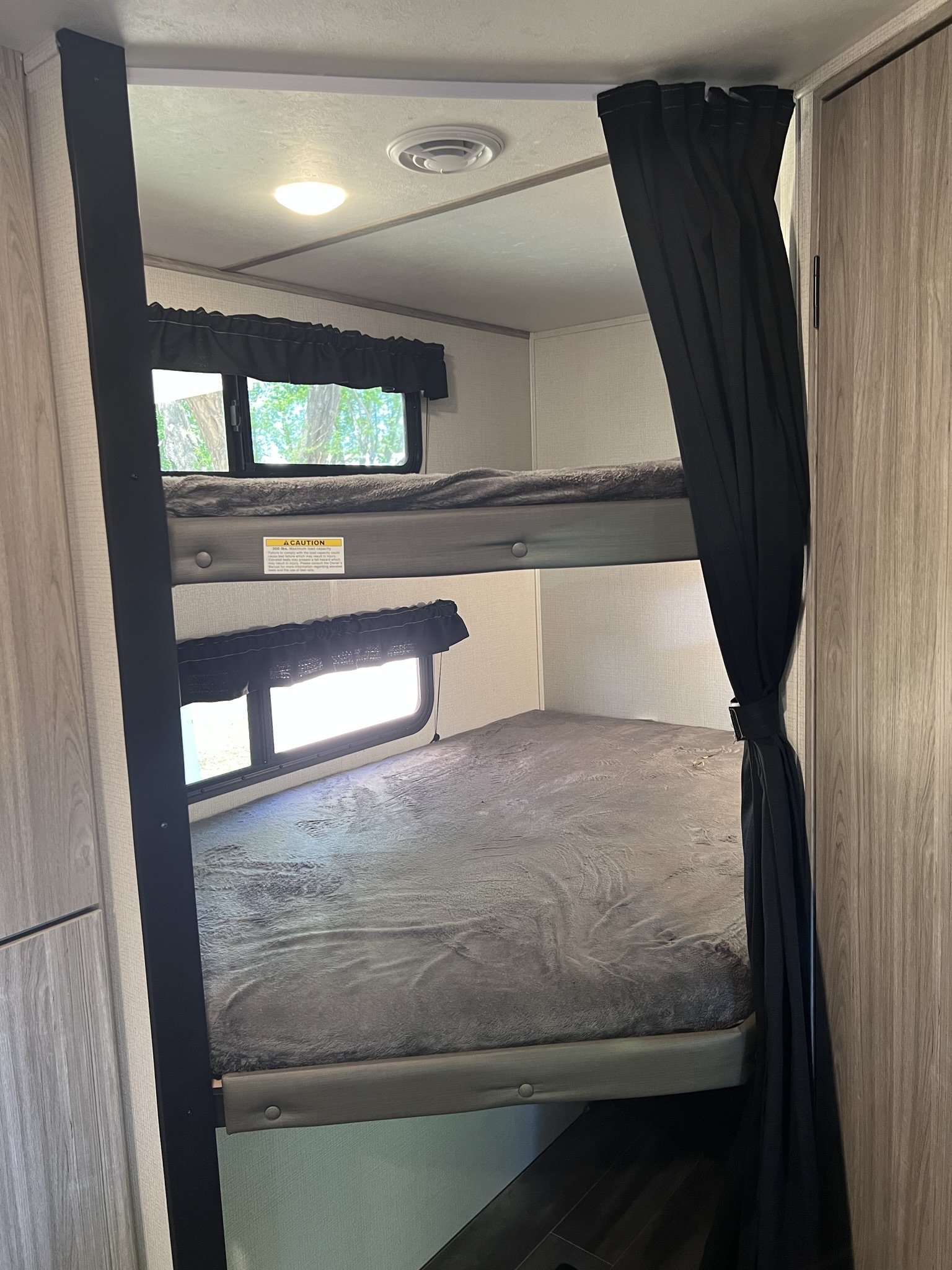 Inside an RV rental, showing cozy bunk beds with windows, blackout curtains, and a visible caution label for safety.. Keystone RV Passport SL 2021