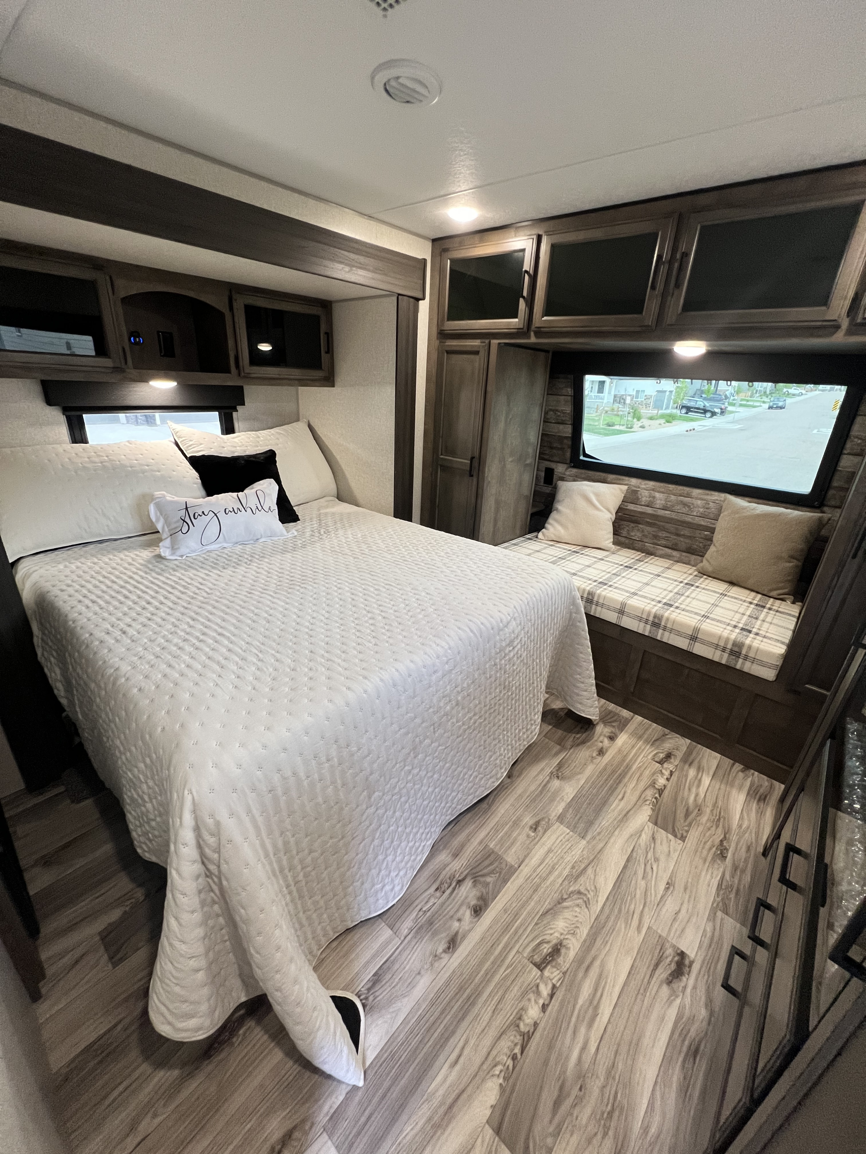 Step into comfort in this modern RV rental bedroom featuring a cozy bed, built-in bench, and stylish wood accents.. Sport Trek Touring Edition 2023