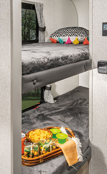 Cozy RV rental interior showcasing bunk beds. The top bunk has a colorful pillow, while the lower bunk holds a tray of snacks, ready for travel.. Sonic Lite 2023