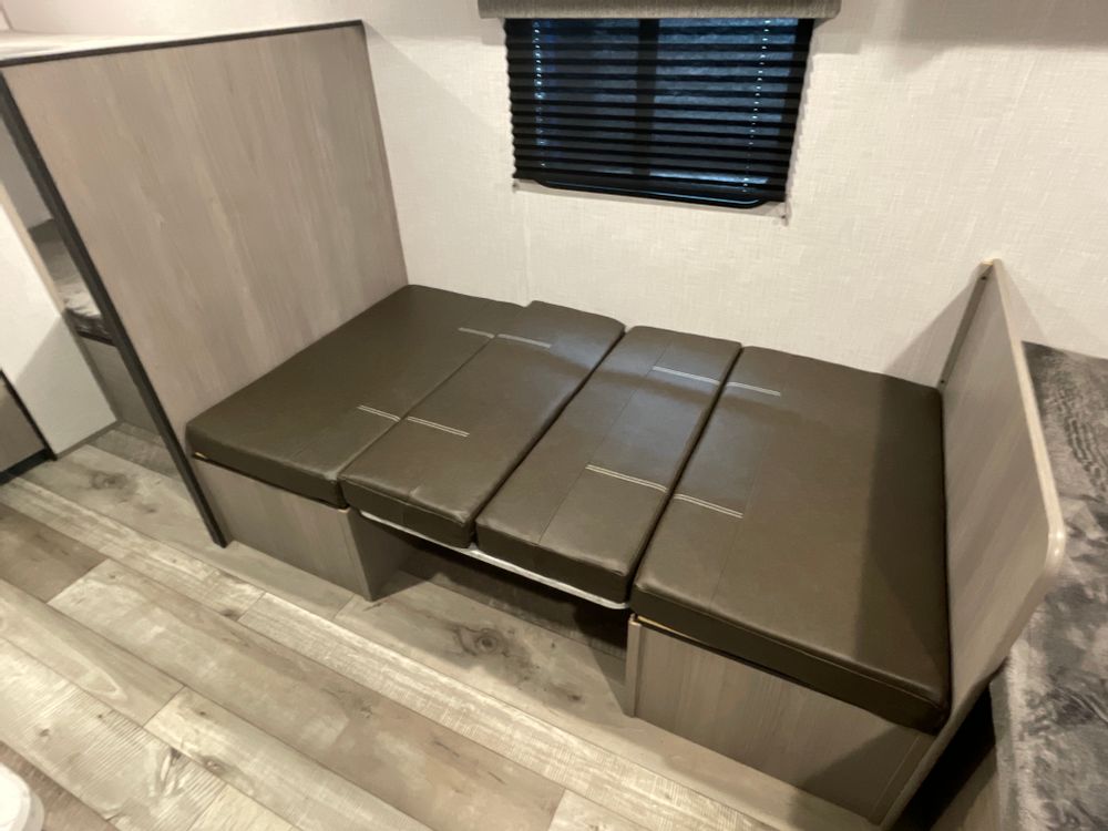 Explore RV rental comfort! Dinette seating with sleek brown cushions, window blinds, and wood-look floor. Converts to bed.. Dutchmen Coleman Lantern LT 2023