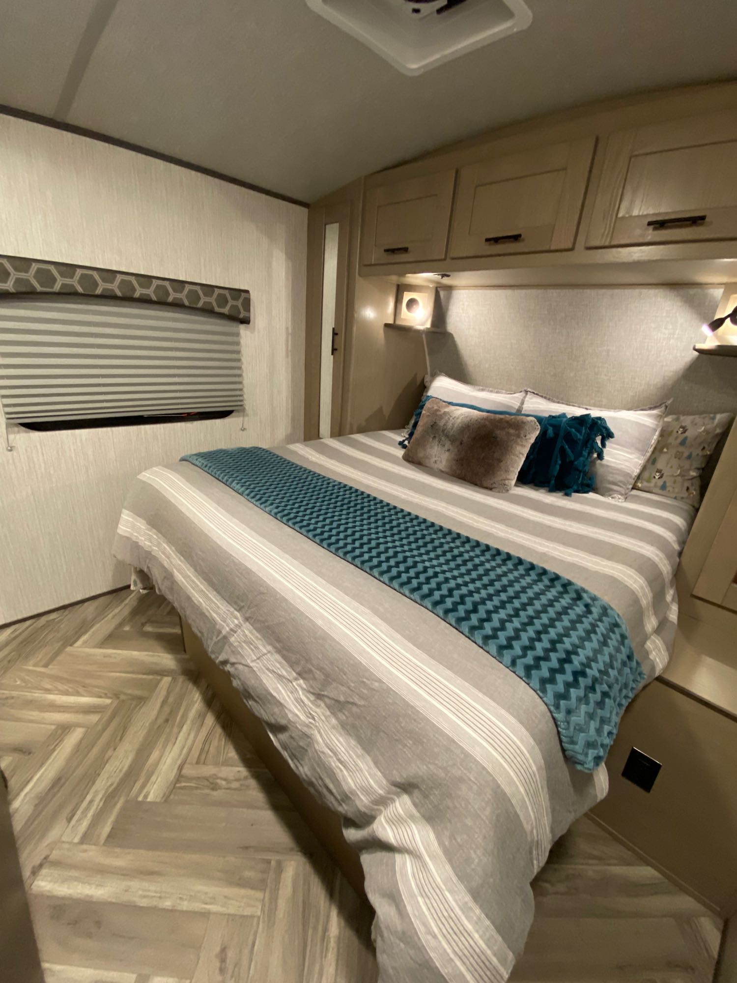 Cozy RV rental bedroom features a queen bed with striped bedding, overhead cabinets, and warm lighting, ideal for comfortable travel.. Shadow Trailers 277BHS 2020