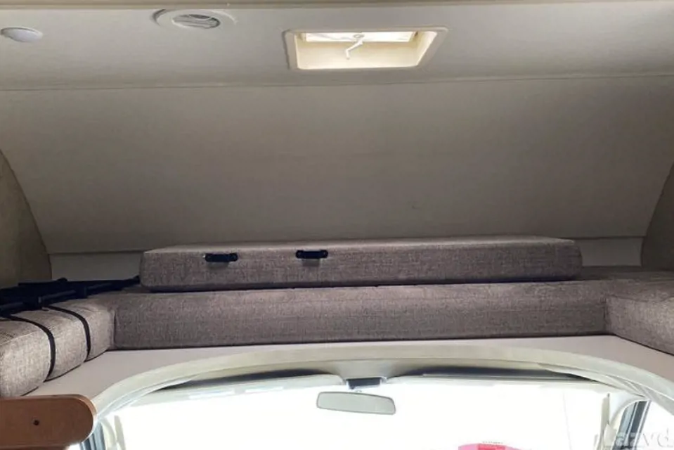 Inside an RV rental: View of the cozy cab-over bunk, featuring comfortable gray cushions and a roof vent for light.. Winnebago Spirit 2018