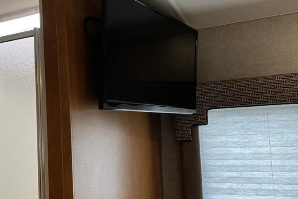 Compact RV rental space featuring a mounted TV, frosted glass shower door, and window with patterned valance.. Winnebago Spirit 2018