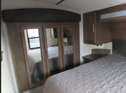 Discover this comfortable RV rental bedroom, featuring a large mirrored closet, cozy bed, and overhead storage. Ideal for road trips.. Keystone RV Cougar 2022