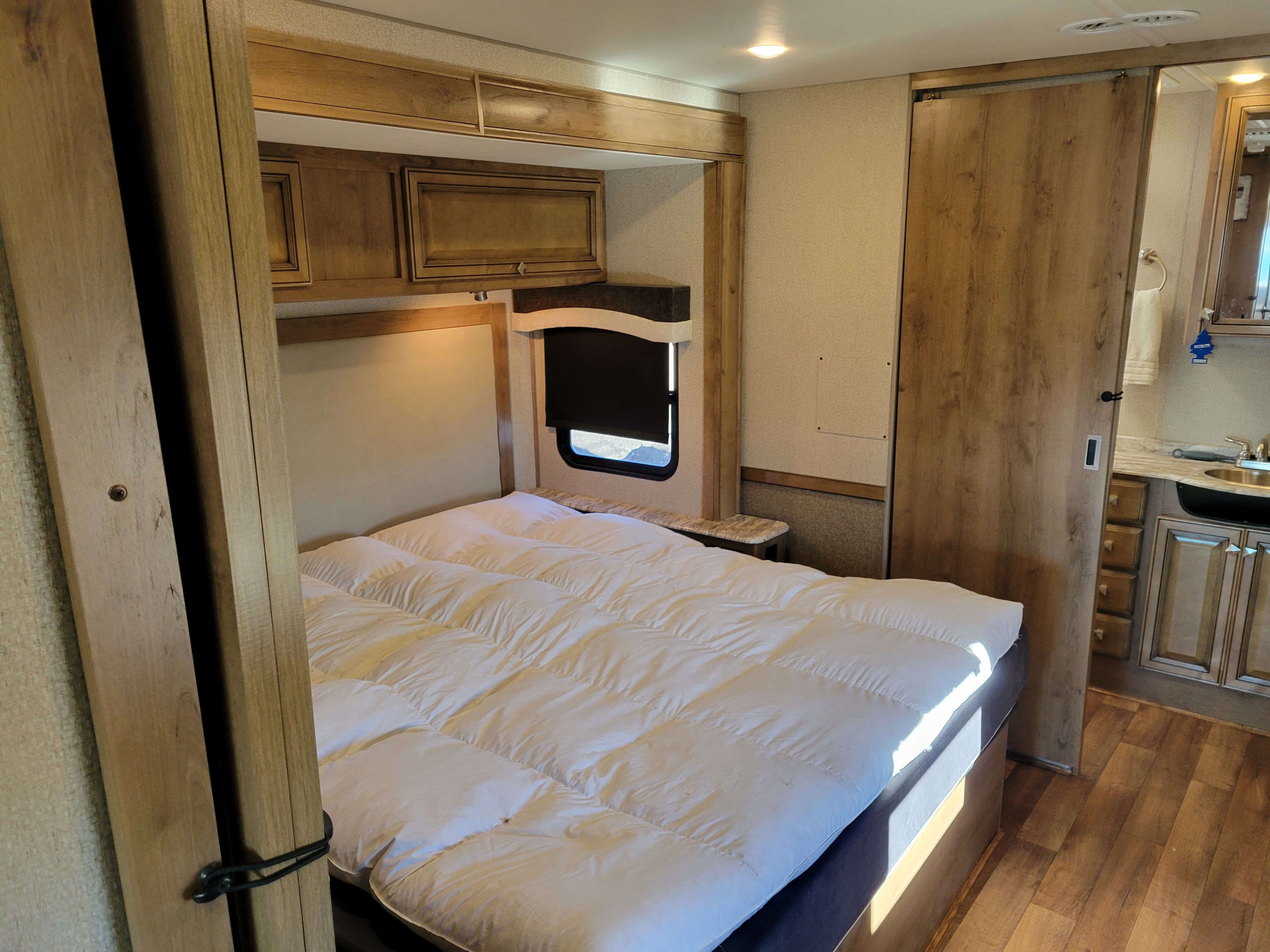 Comfortable RV rental bedroom with a white duvet, overhead cabinets, and sliding door to the bathroom area.. Fleetwood Flair 32S 2019