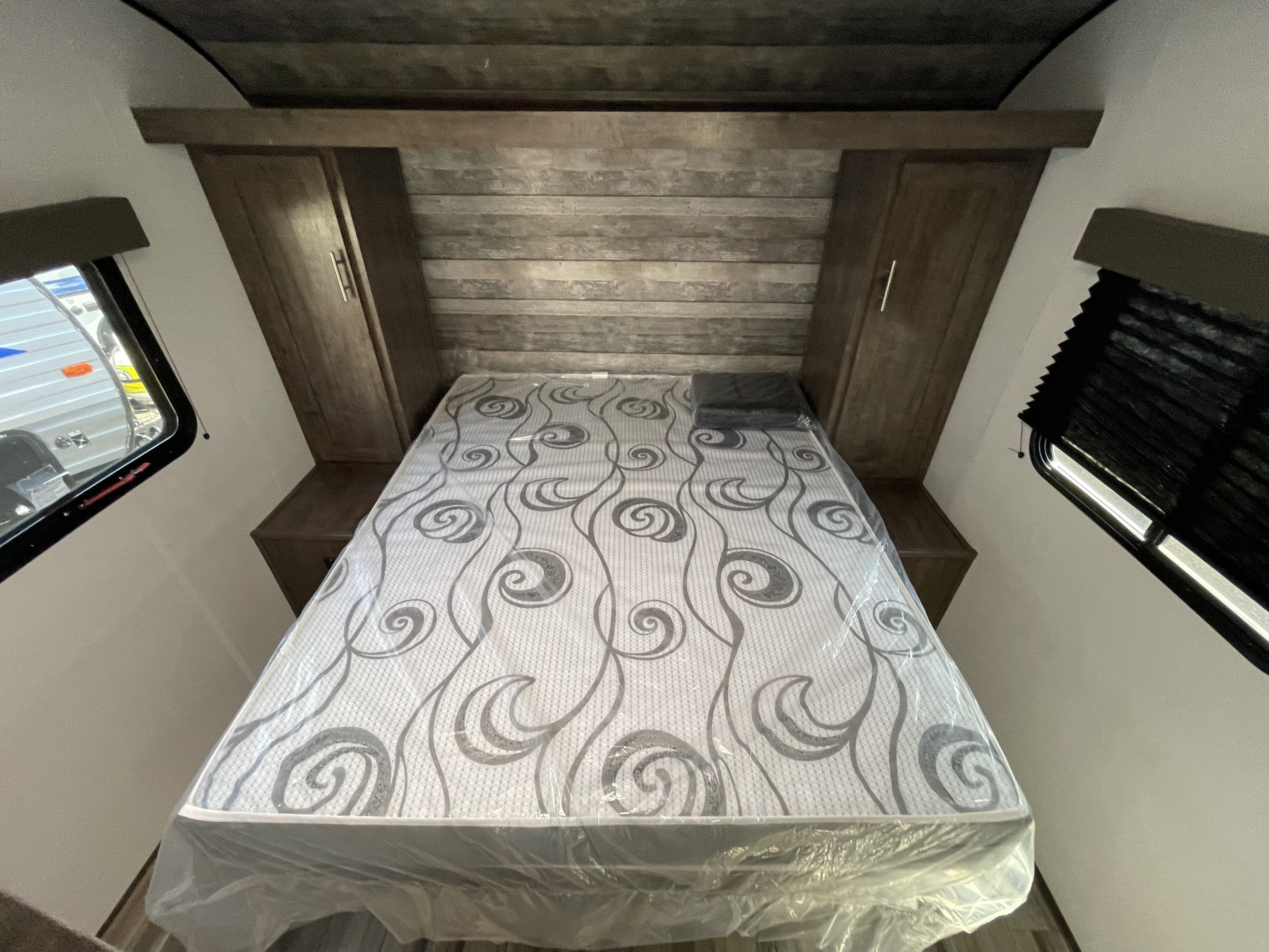 Clean RV rental bedroom: new mattress in plastic, built-in cabinets, and wood-look headboard. Ready for adventure.. Riverside Rv Retro 2022