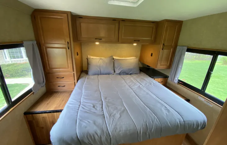 Cozy RV rental bedroom with a comfy bed, overhead storage, and windows, providing a comfortable space for travel.. Thor Majestic 2018