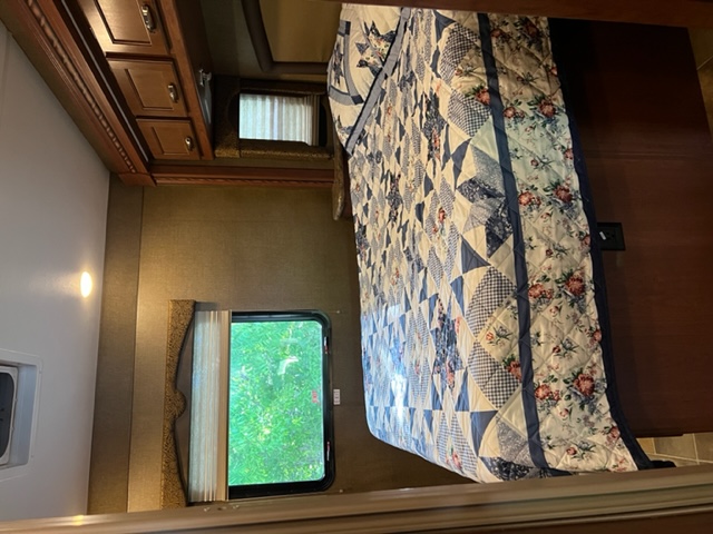 Cozy RV rental bedroom with a blue patterned quilt, wooden cabinets, wall-mounted TV, and a scenic window view.. Ford Freedom Elite 2016